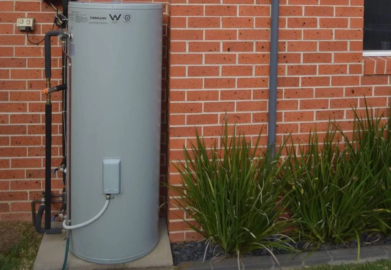A Grey Water Heater Is Sitting Outside of A Brick Building — Medowie Plumbing & Gas In Medowie, NSW