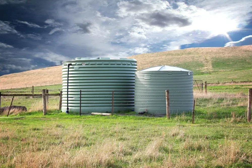 Two Water Tanks Are Sitting in A Grassy Field — Medowie Plumbing & Gas In Medowie, NSW