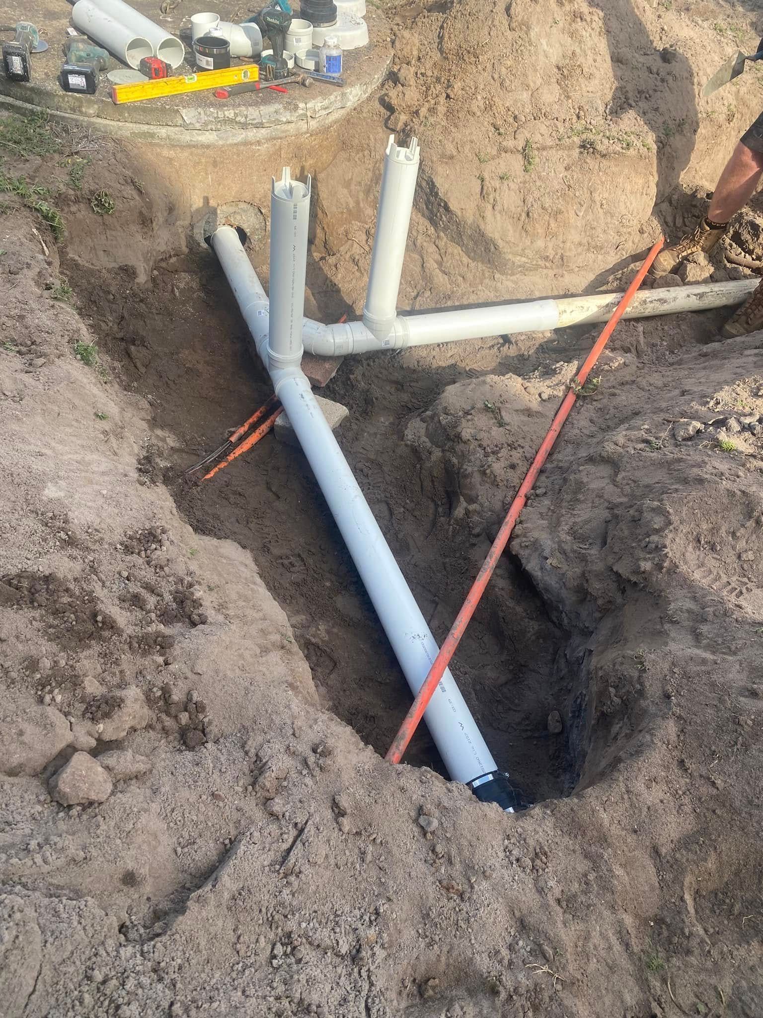 A Pipe Is Being Installed in The Dirt Next to A Fence — Medowie Plumbing & Gas In Medowie, NSW