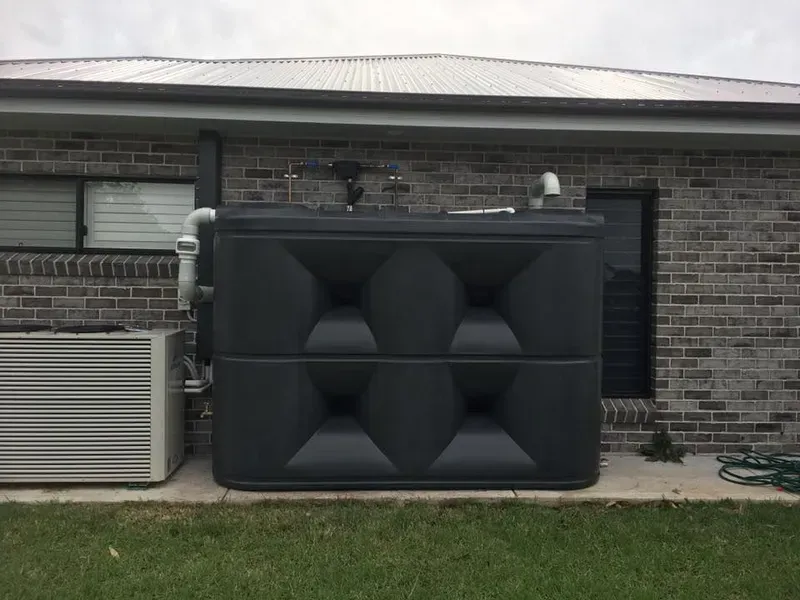 A Black Water Tank Is Sitting on The Side of A Brick House — Medowie Plumbing & Gas In Medowie, NSW