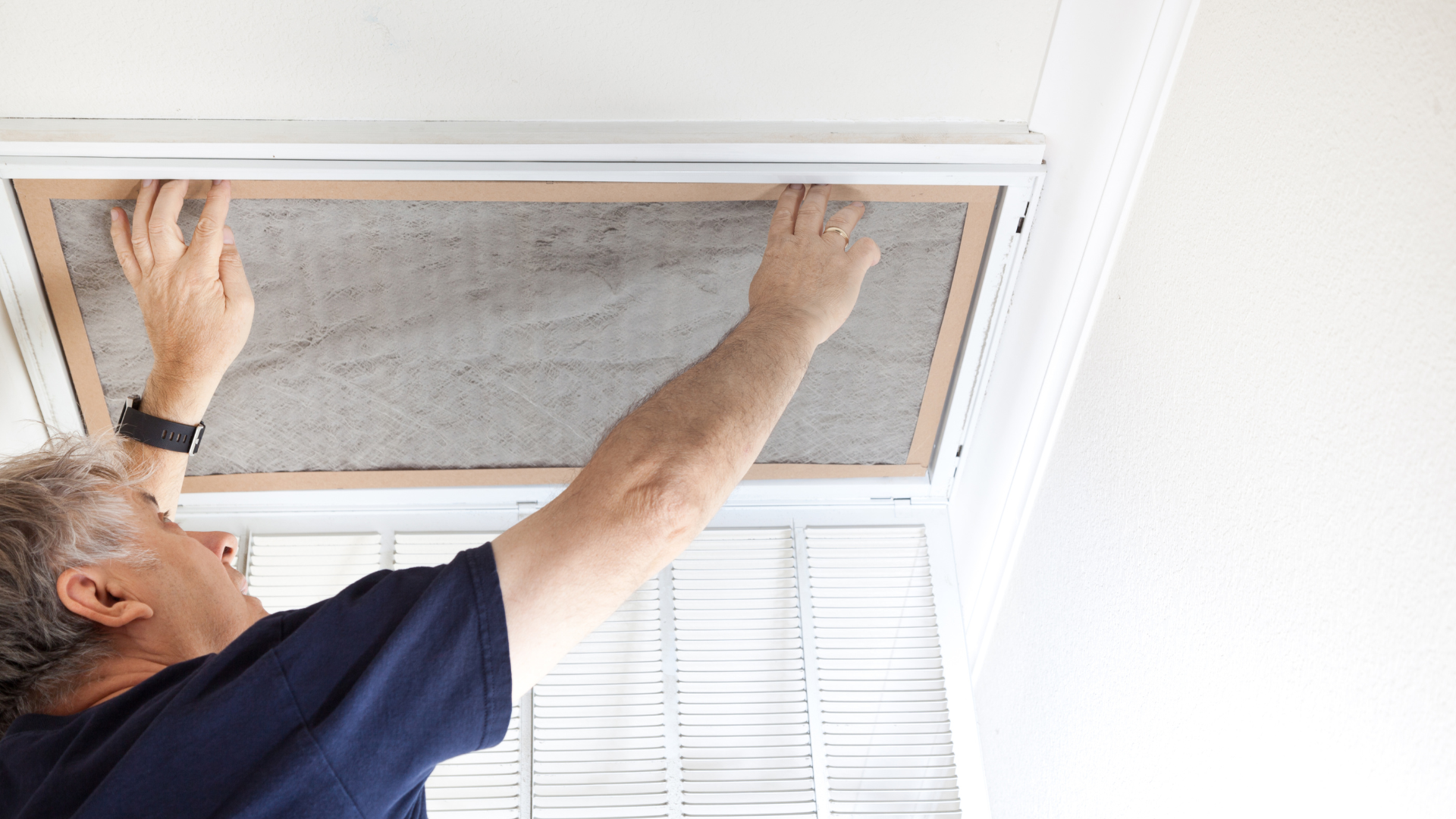 A man is cleaning an air filter on the ceiling of a room.