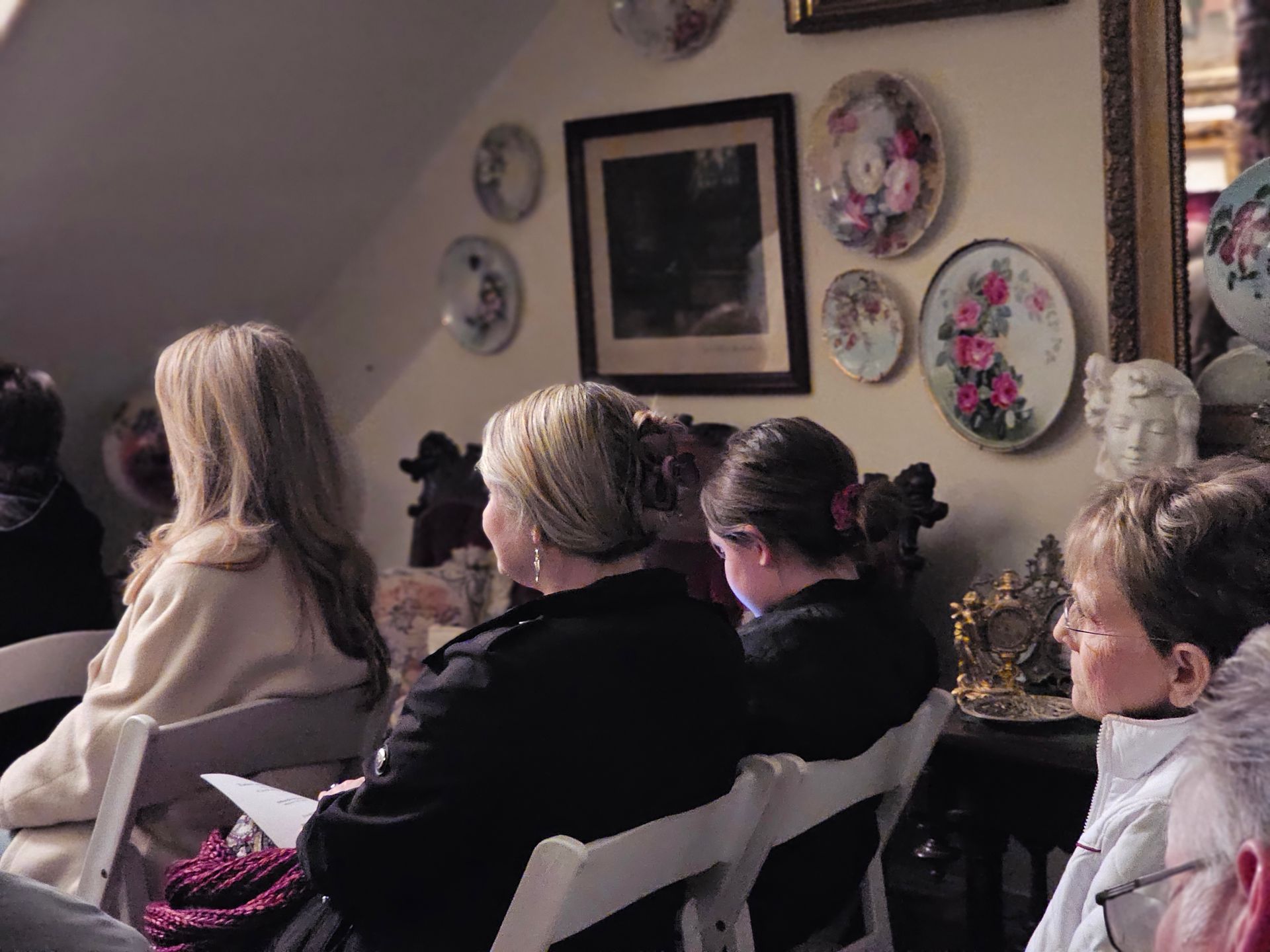 A group of people are sitting in chairs in front of a wall with plates on it