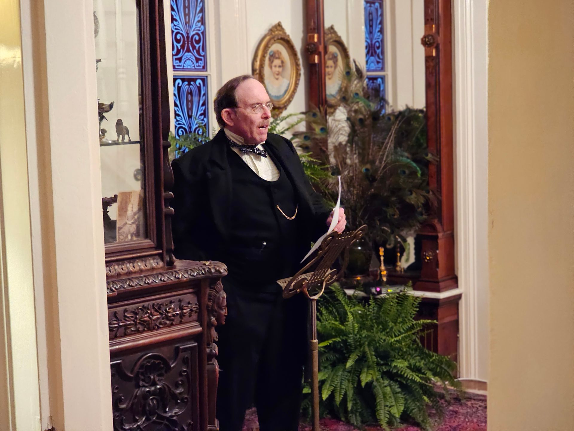 A man in a tuxedo is standing in a room reading a book.