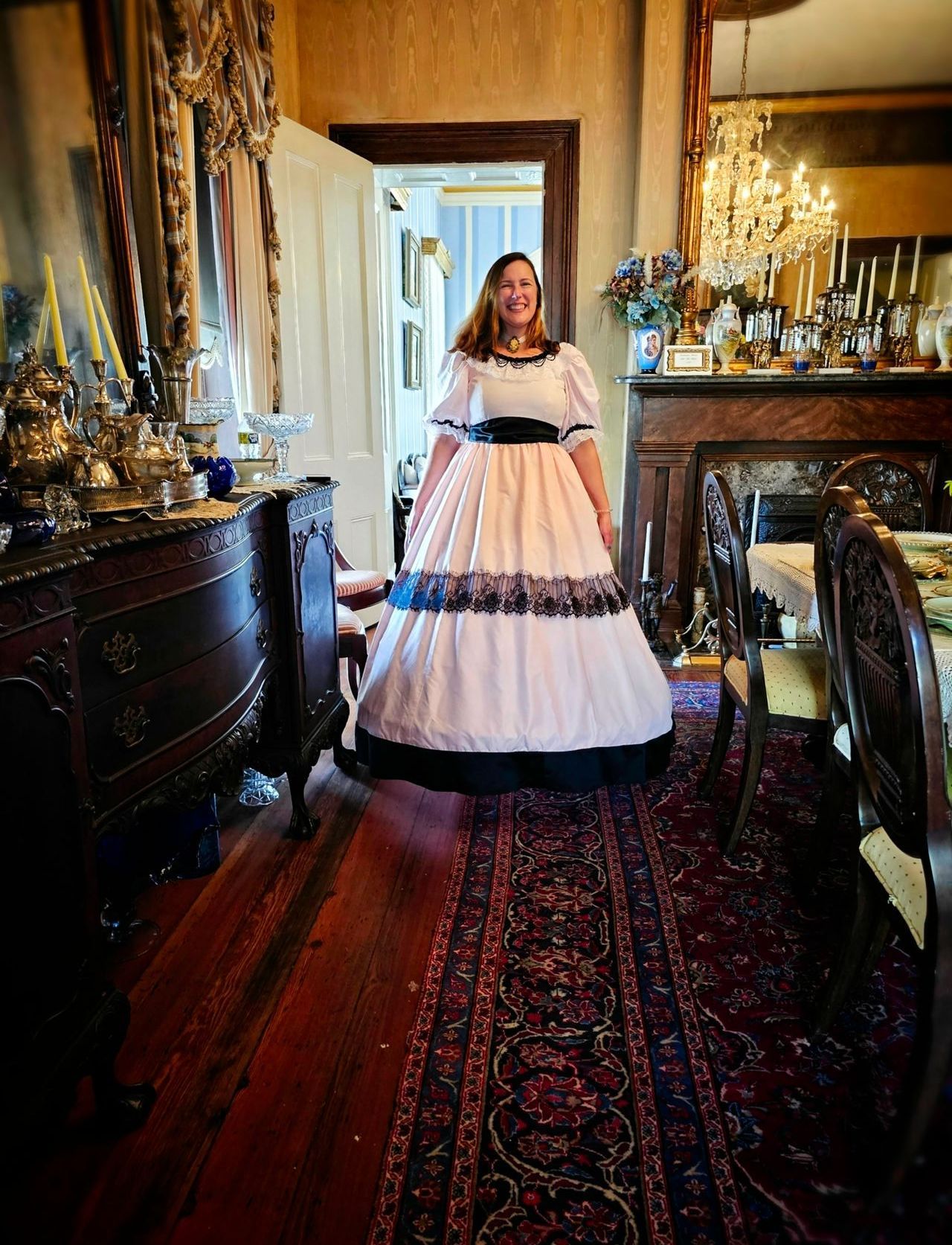 A woman in a white dress is standing in a dining room.