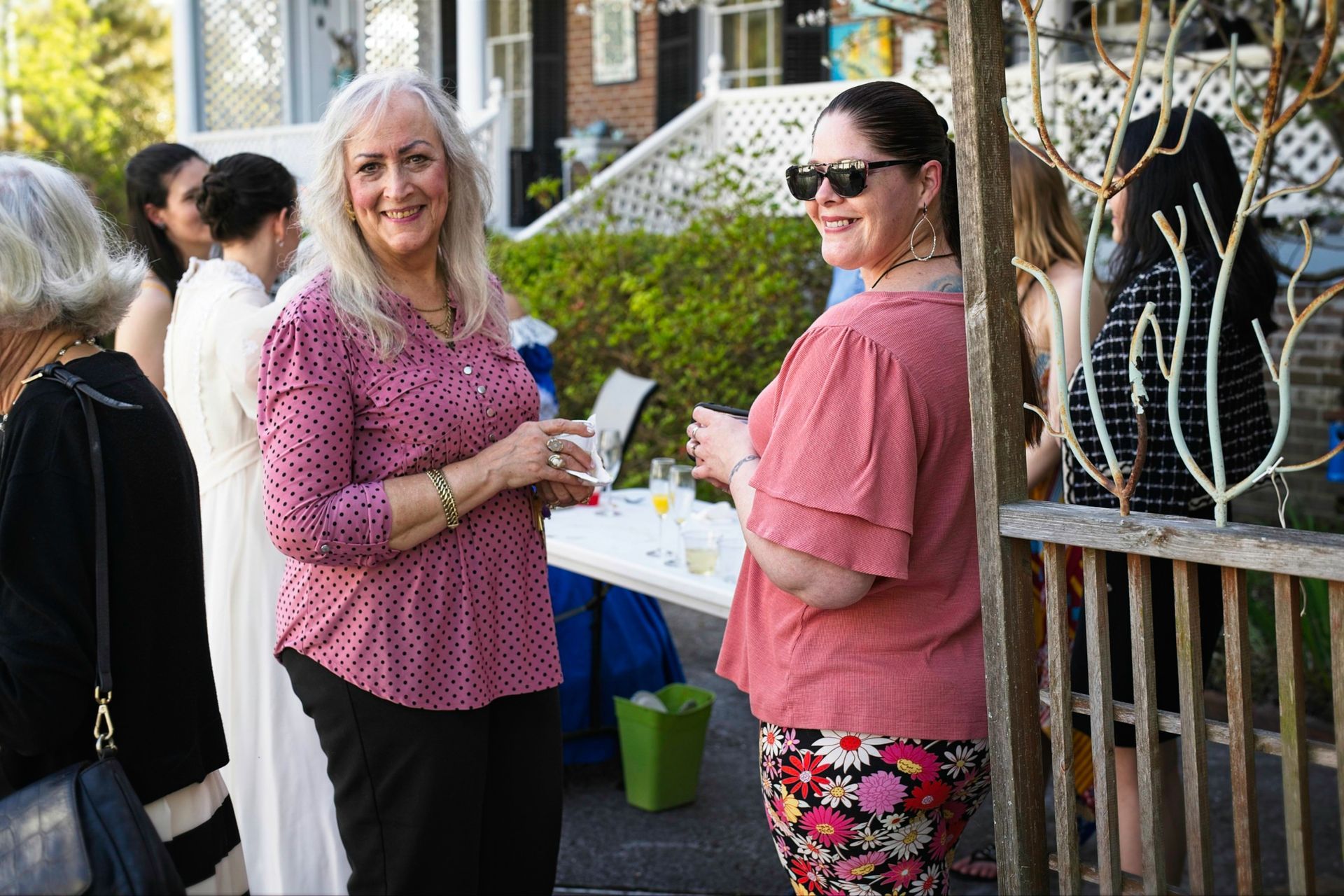 Two women are standing next to each other in front of a fence.