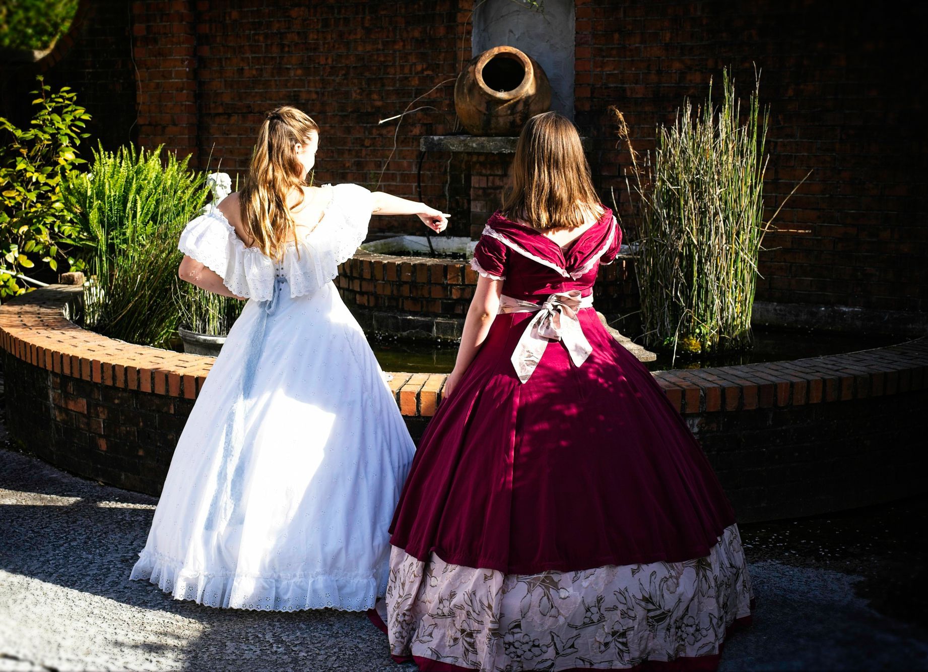 Two women in dresses are standing next to each other in front of a fountain.