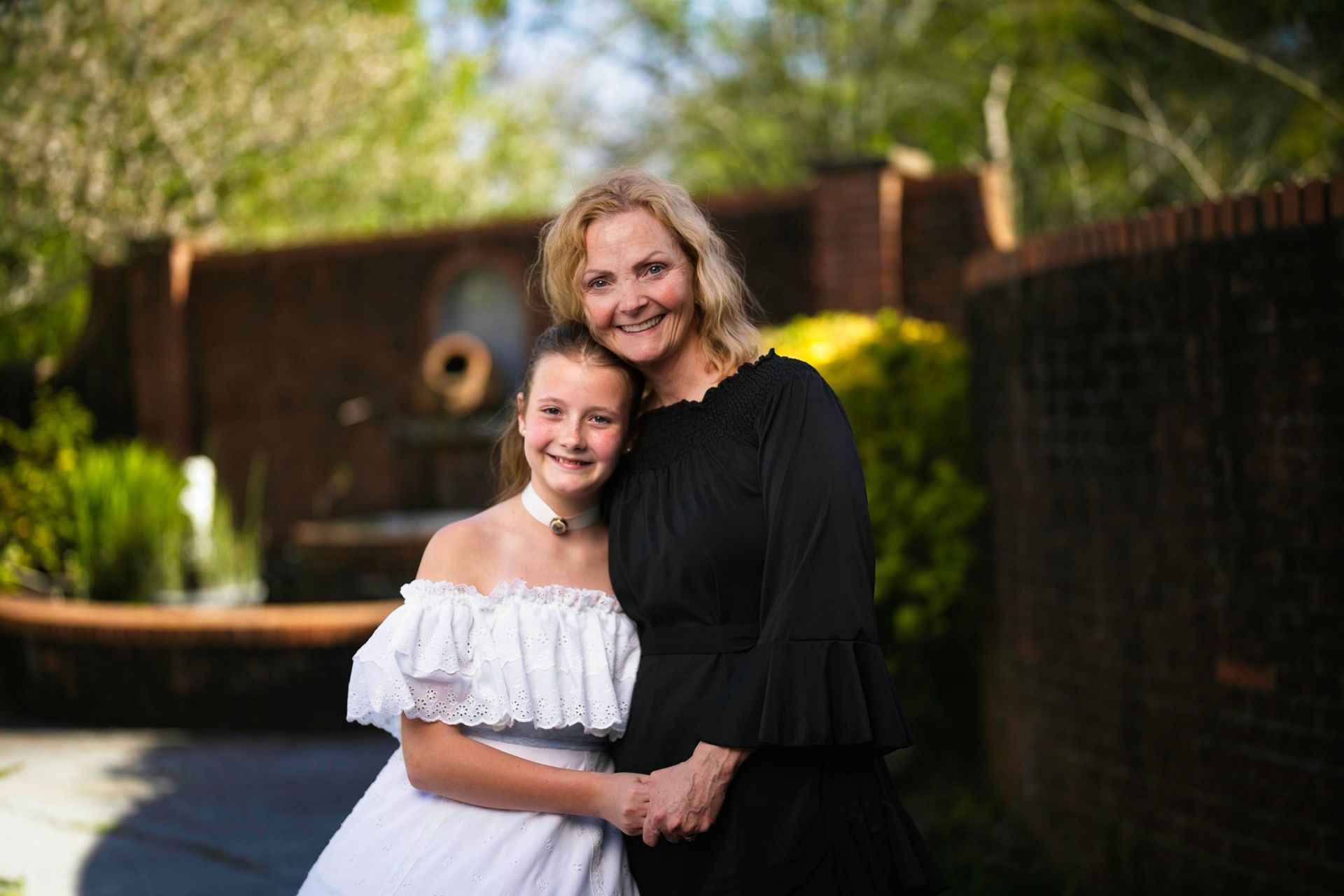 A woman in a black dress is standing next to a girl in a white dress.