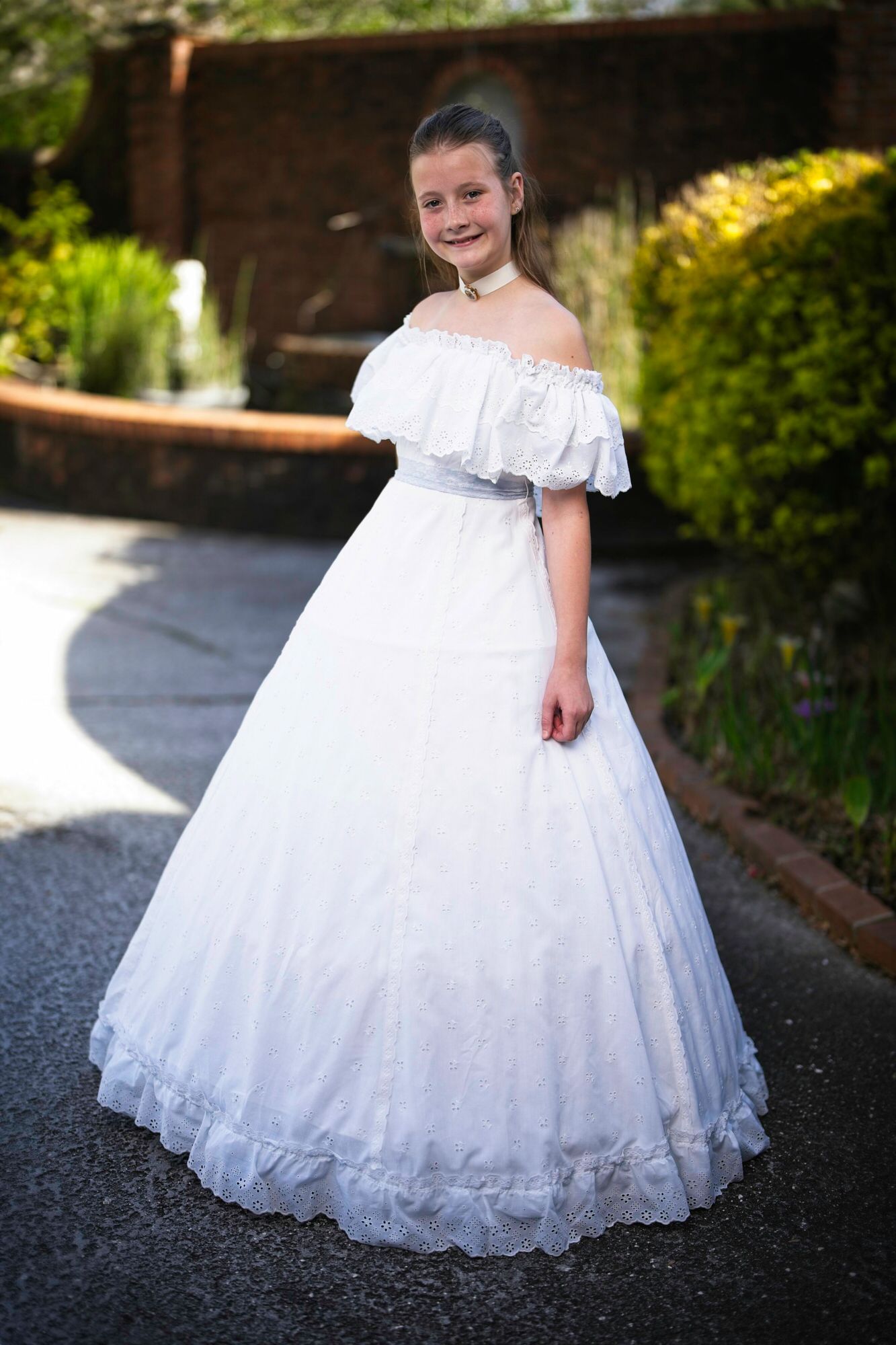 A little girl in a white dress is standing in front of a fountain.