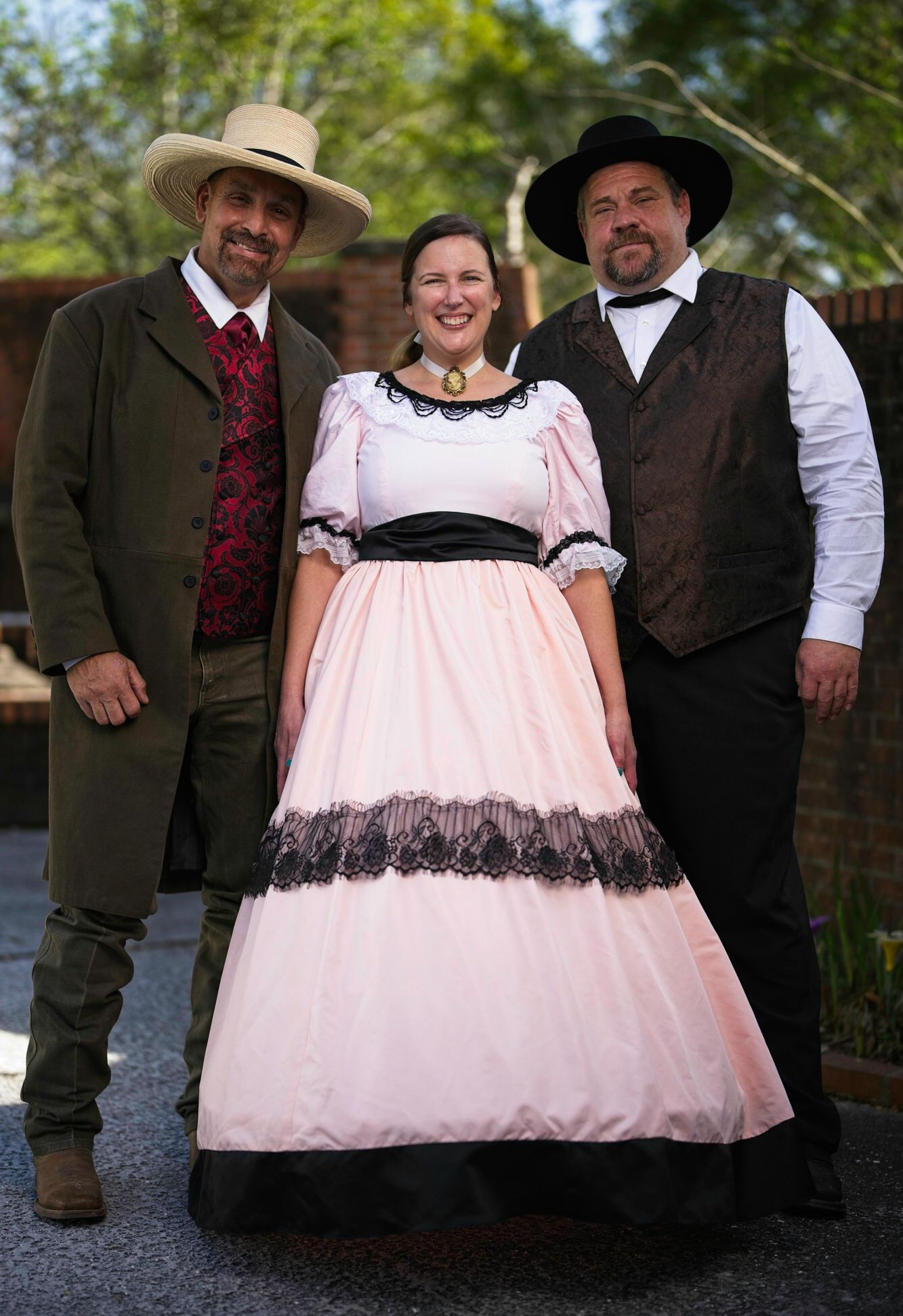 A woman in a pink dress is standing between two men in cowboy hats.