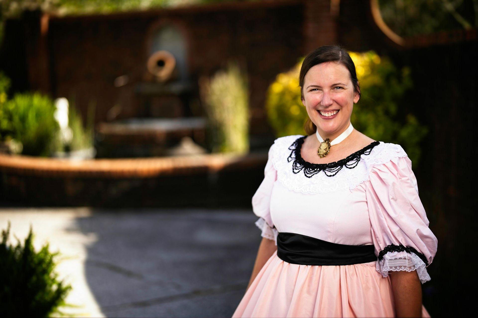 A woman in a pink dress is standing in front of a fountain.