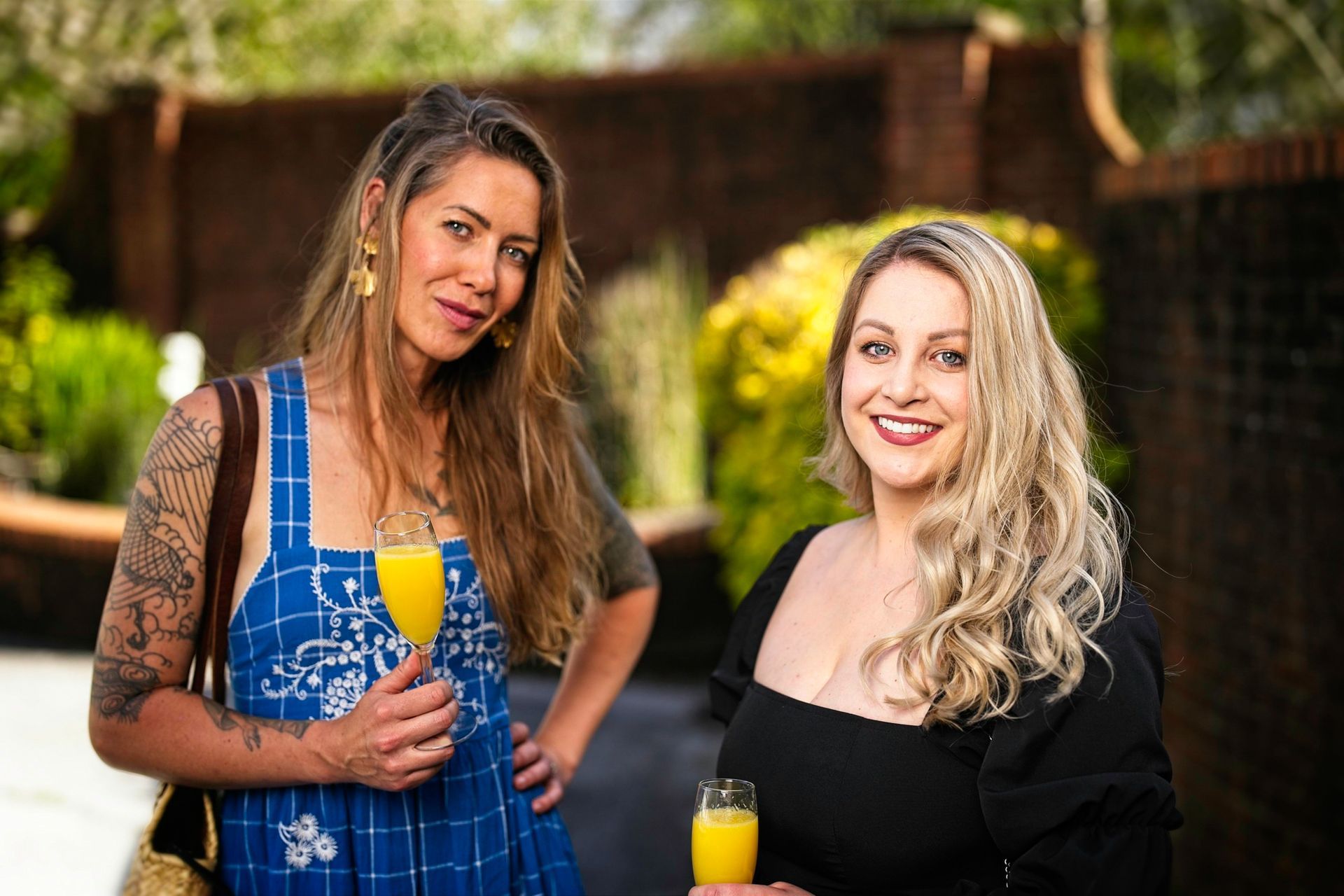 Two women are standing next to each other holding glasses of orange juice.