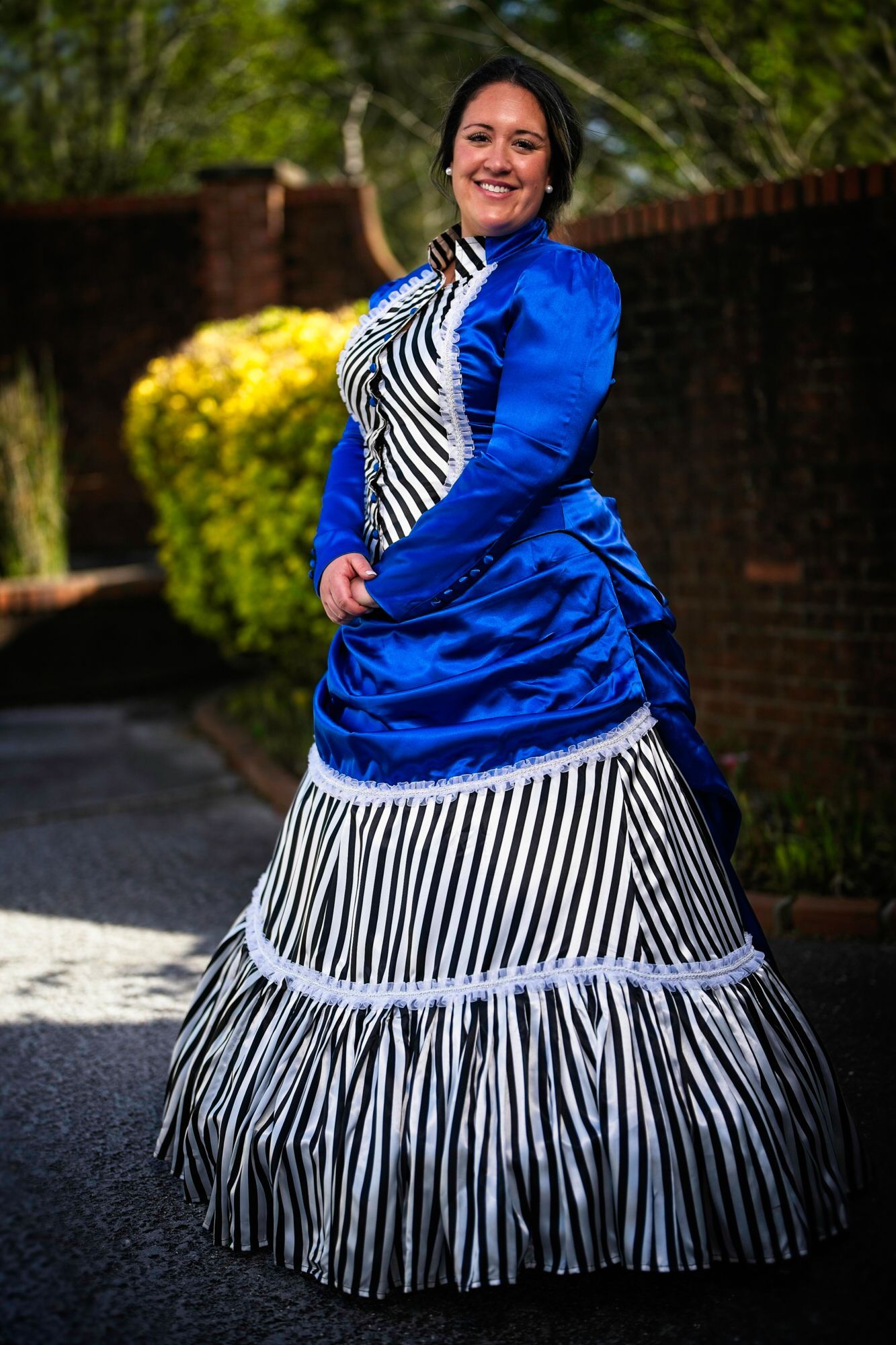 A woman in a blue and white striped dress is standing in front of a brick wall.