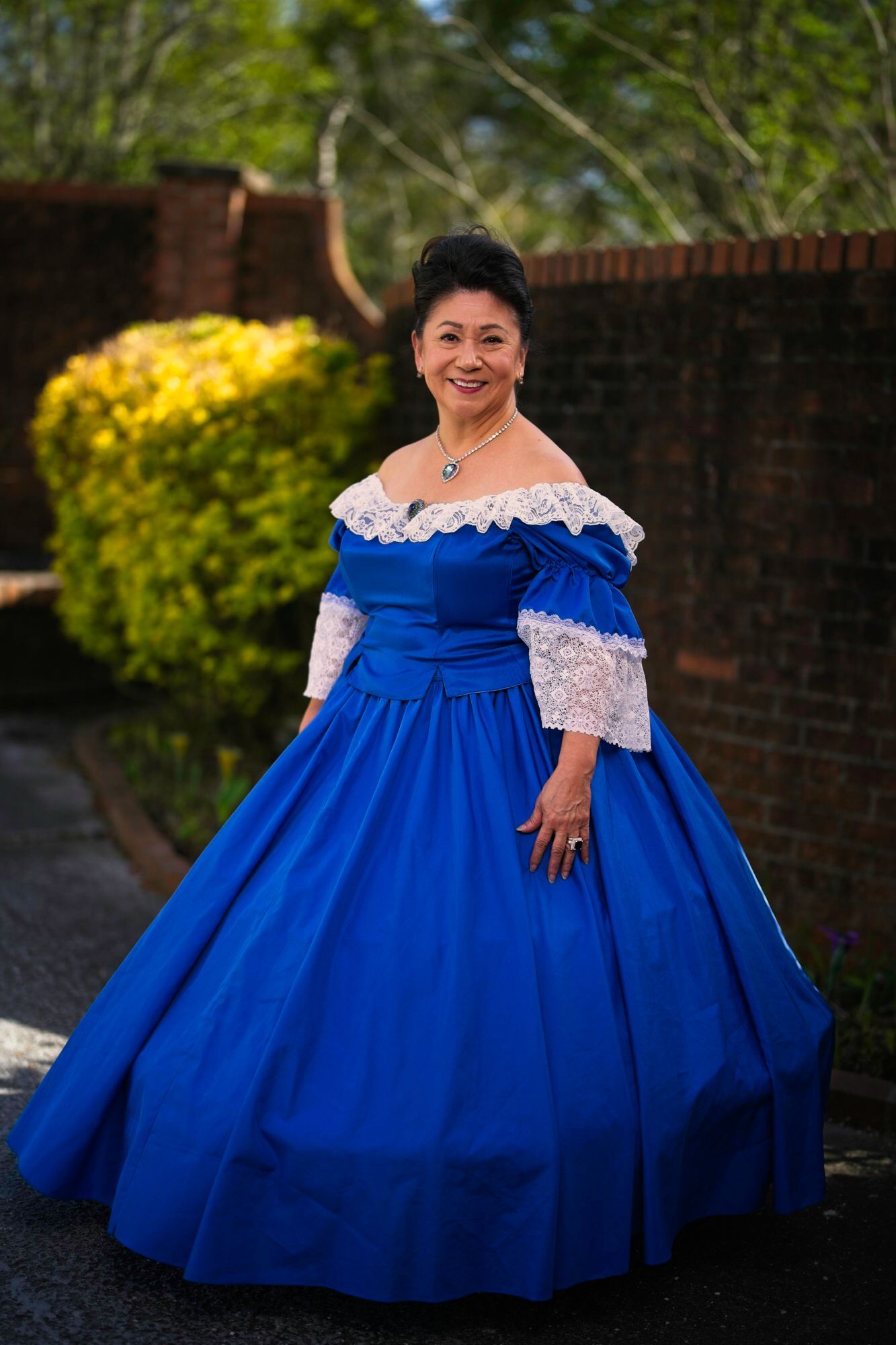 A woman in a blue dress is standing in front of a brick wall.