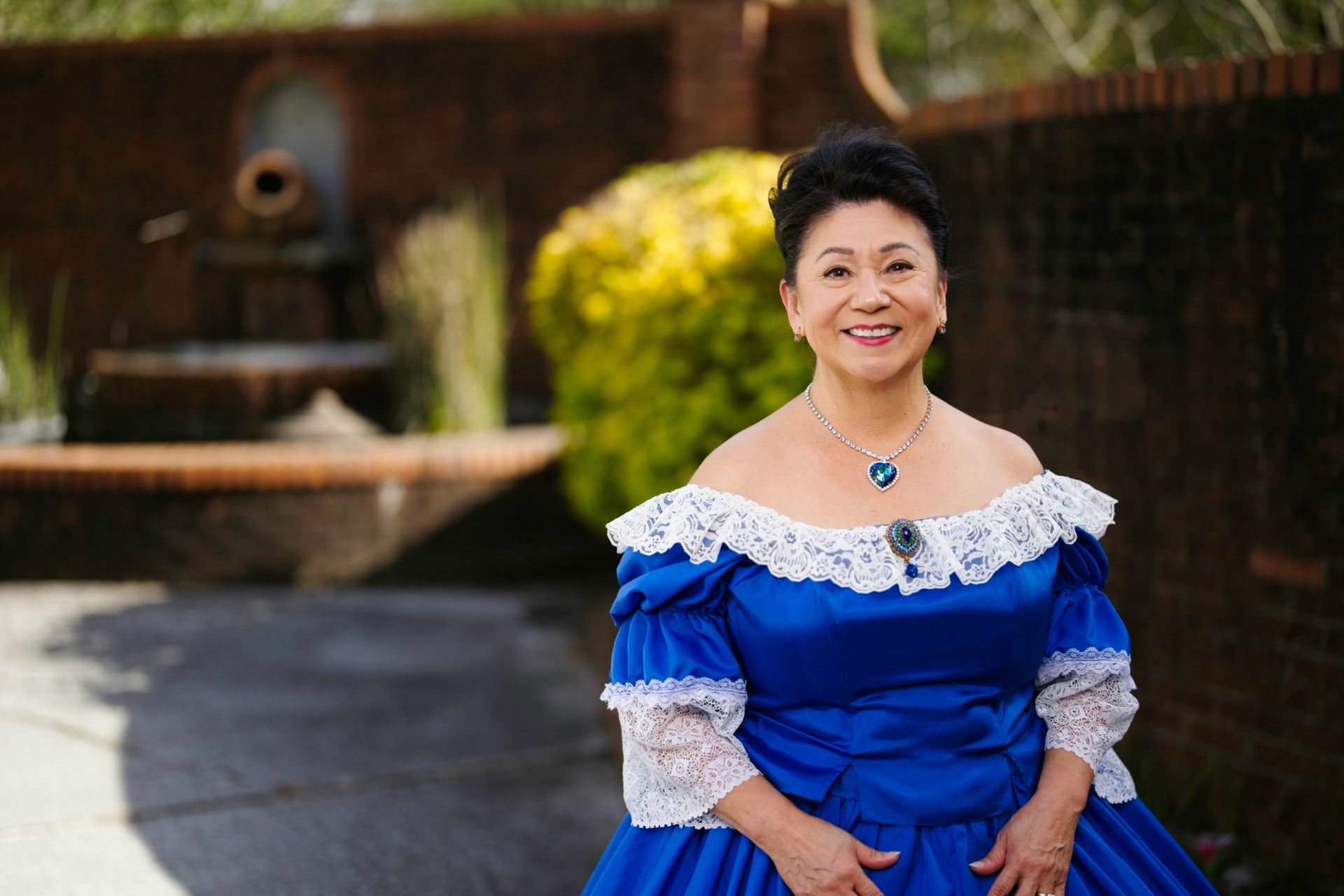 A woman in a blue and white dress is standing in front of a fountain.