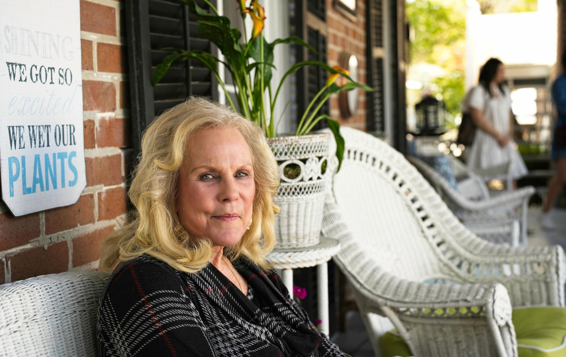 A woman is sitting on a porch next to a sign that says `` we got our plants ''.