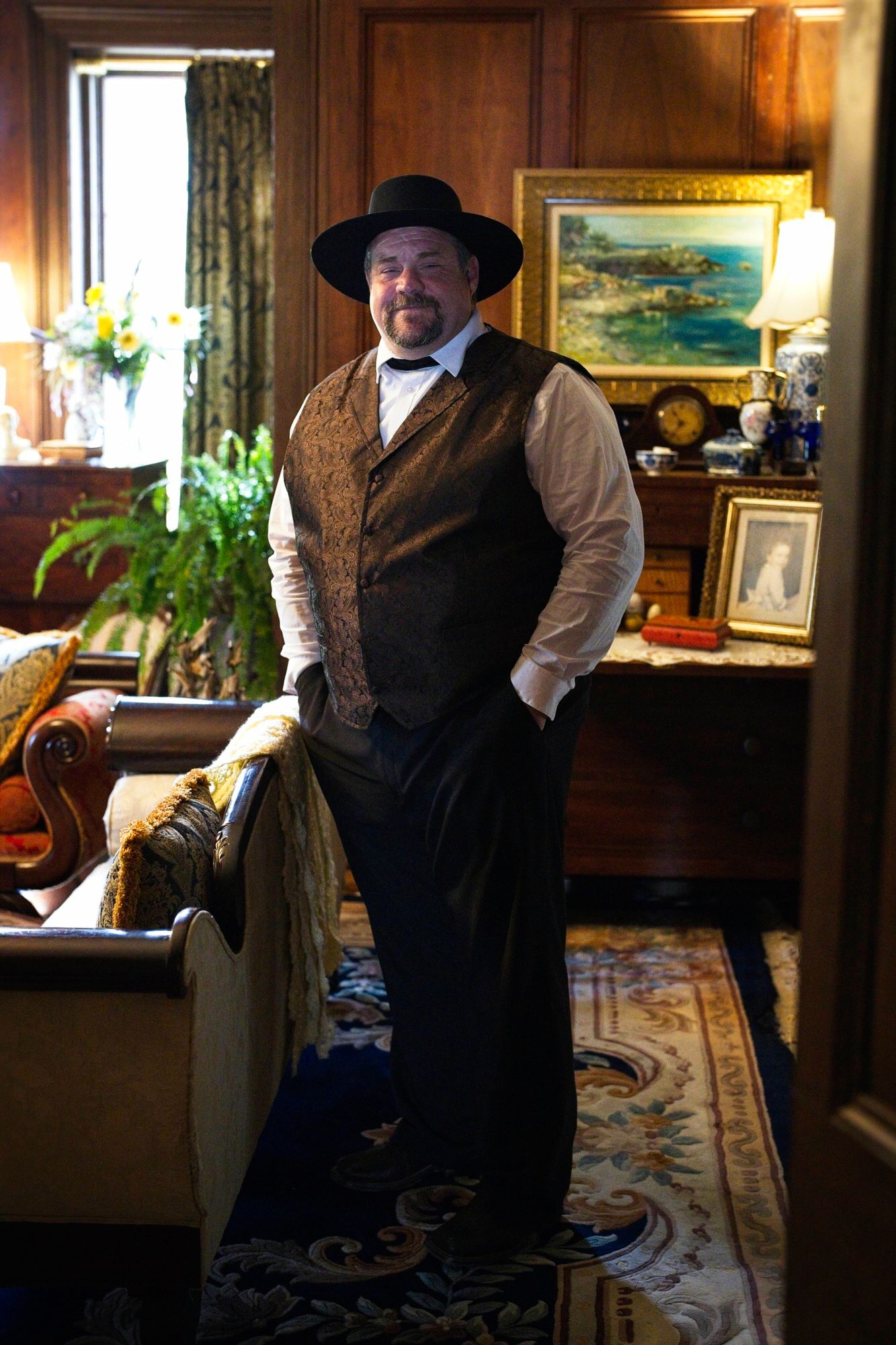 A man in a hat and vest is standing in a living room.