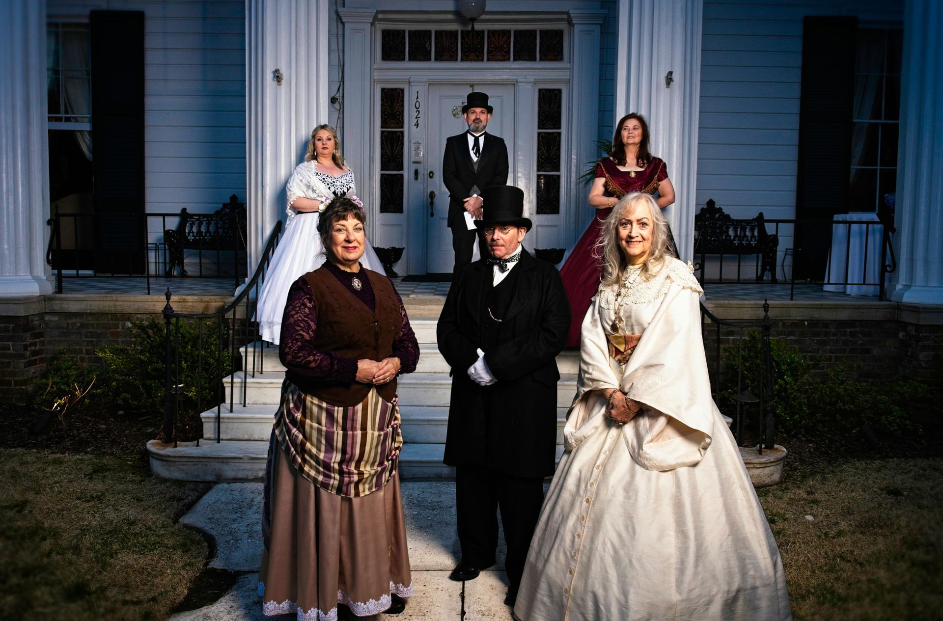 A group of people in historical costumes are posing for a picture in front of a house.