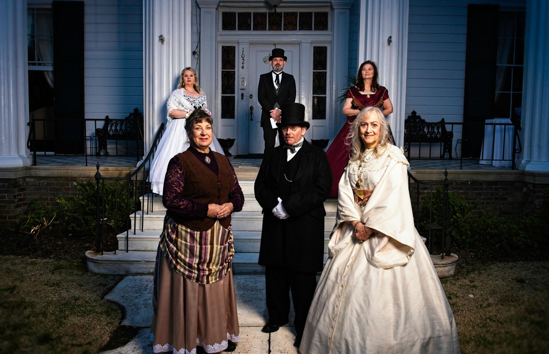 A group of people in historical costumes are posing for a picture in front of a house.