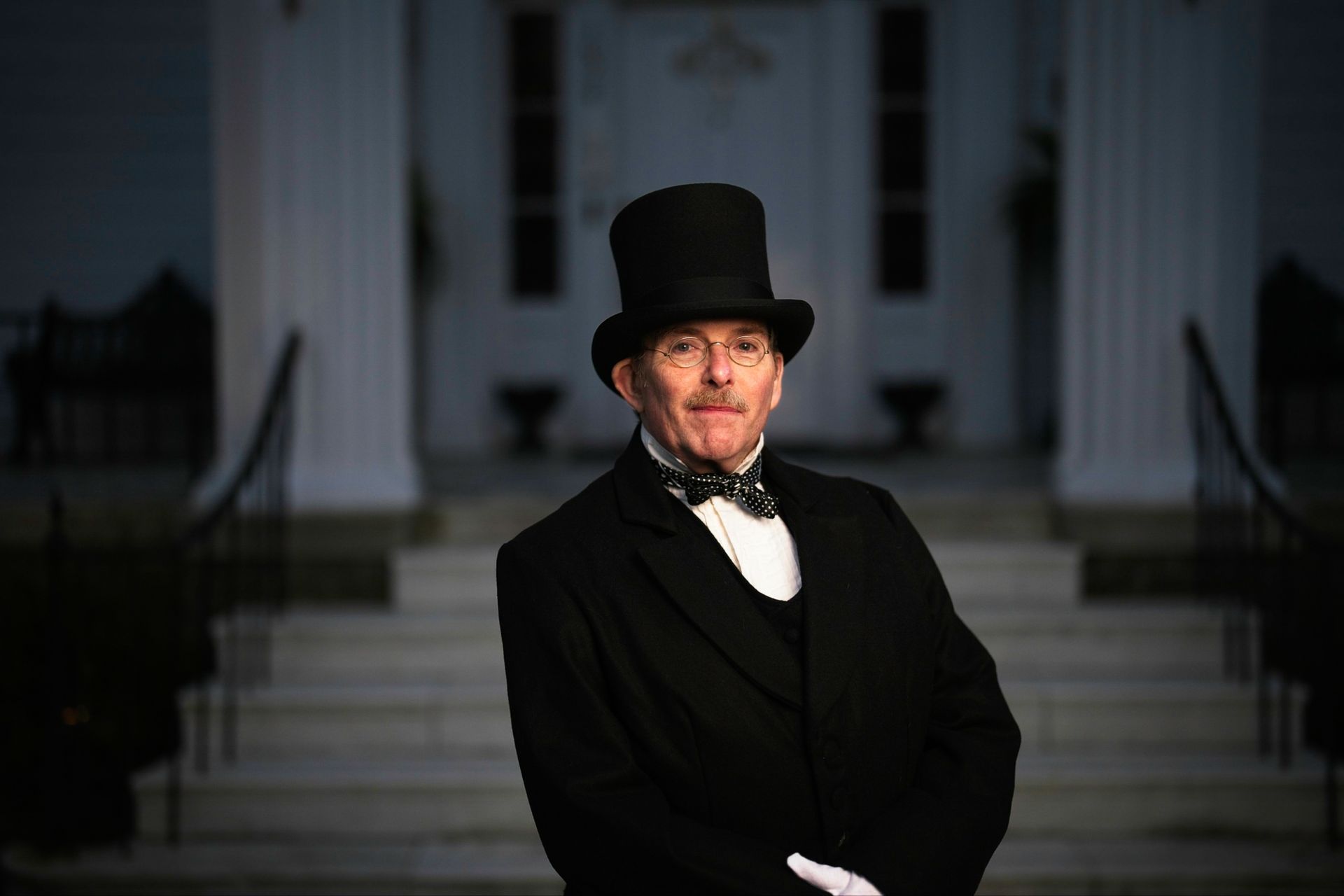 A man in a top hat and bow tie is standing in front of a building