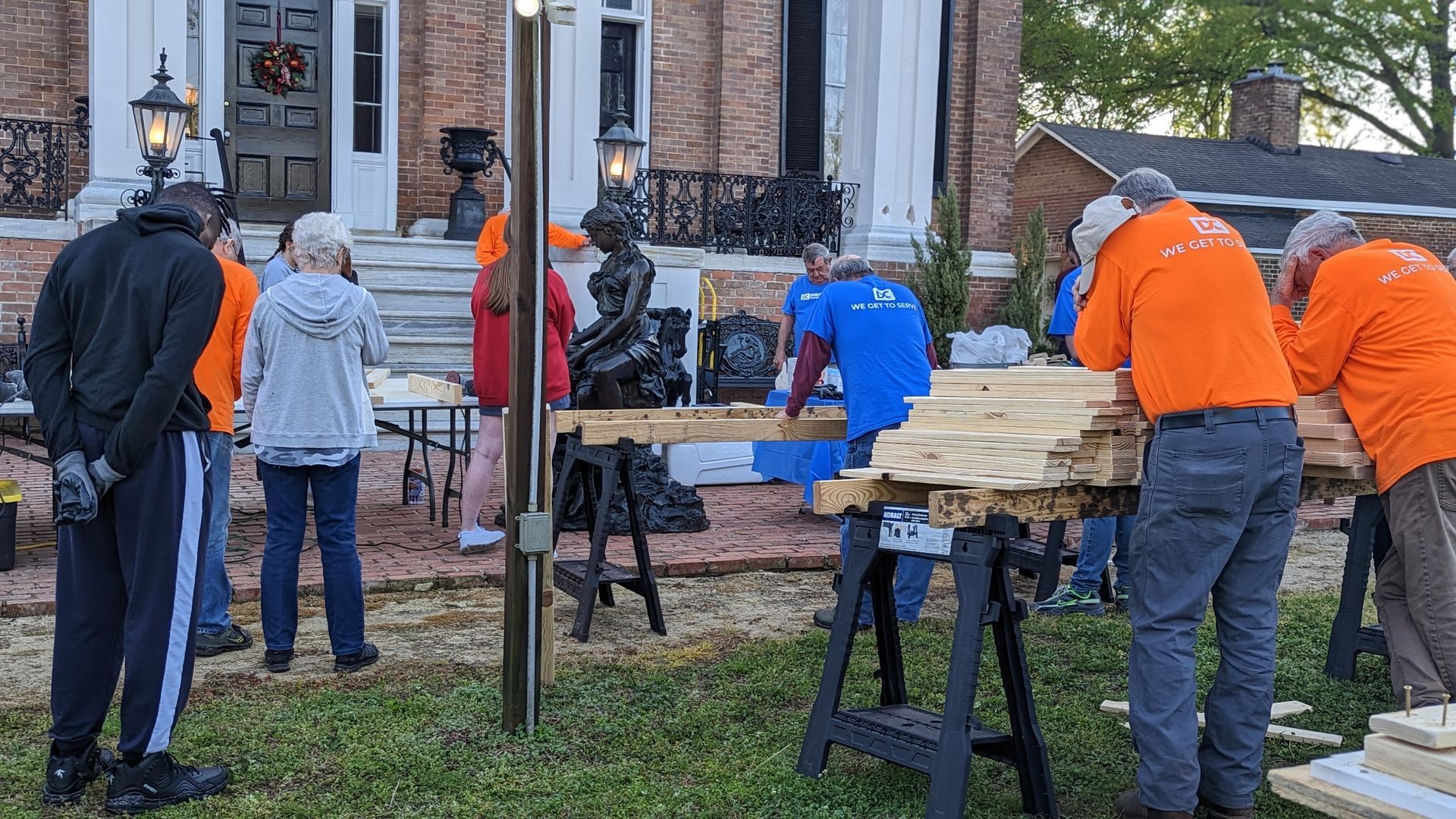 A group of people are working on a wooden table in front of a house.