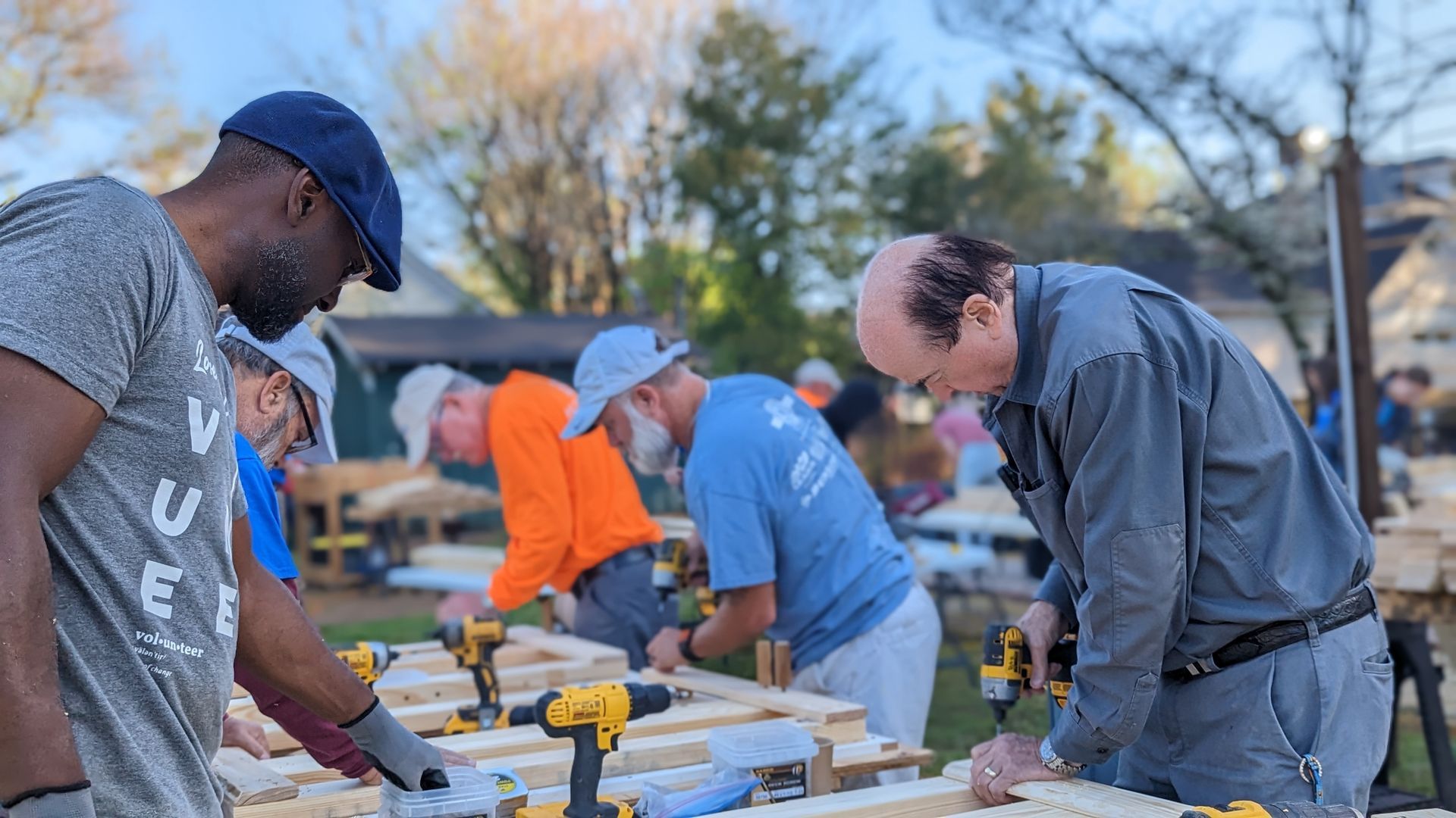 A group of men are working on a wooden table with drills.
