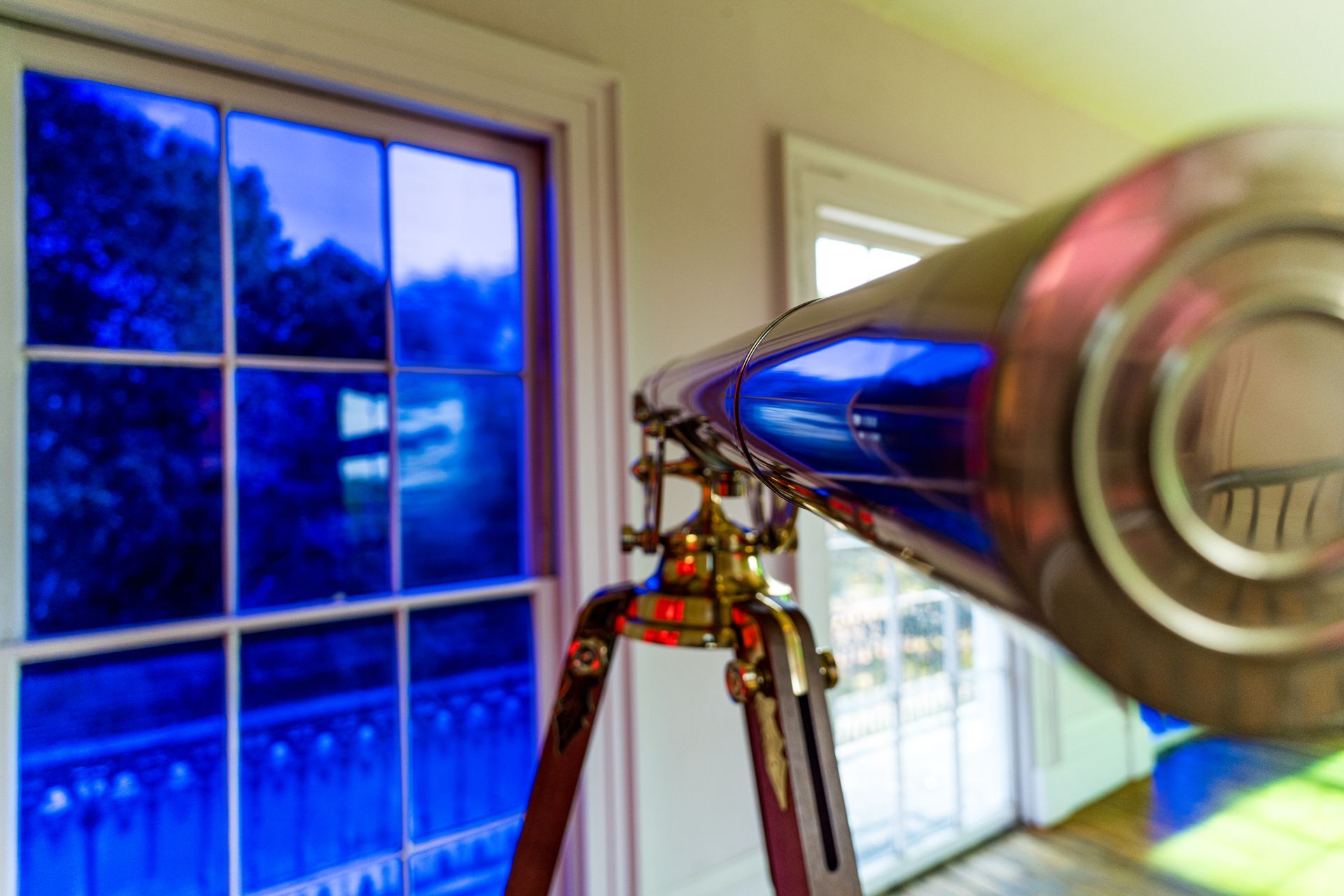 A telescope is sitting in front of a window in a room.