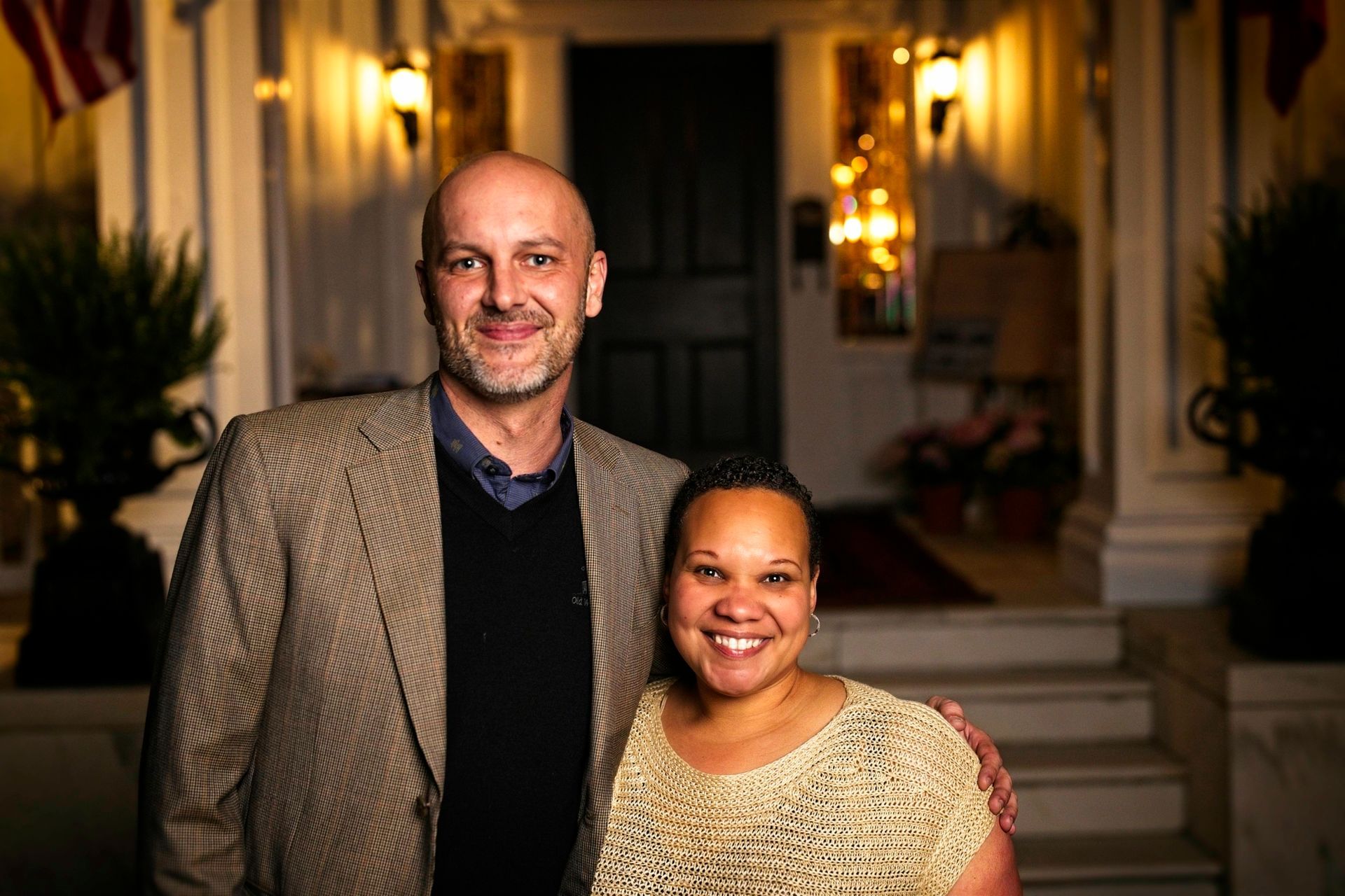 A man and a woman are posing for a picture in front of a house.