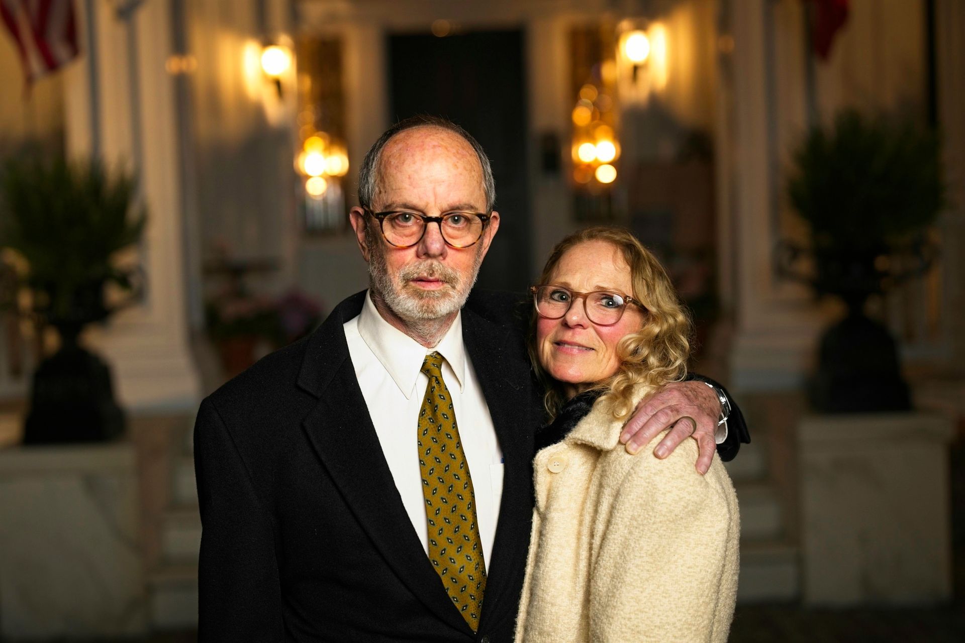 A man in a suit and tie is standing next to a woman in a white coat.