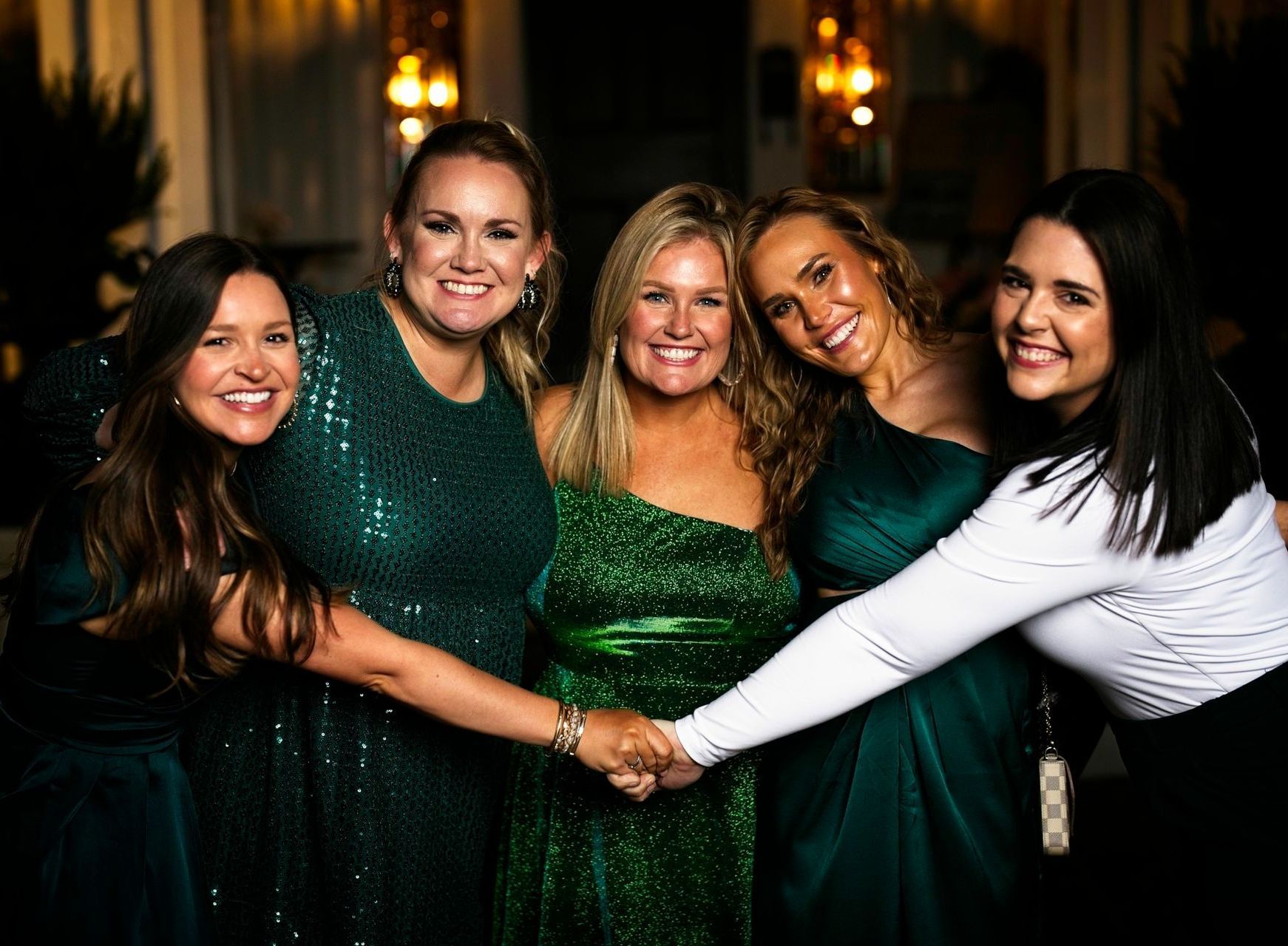 A group of women in green dresses are holding hands.