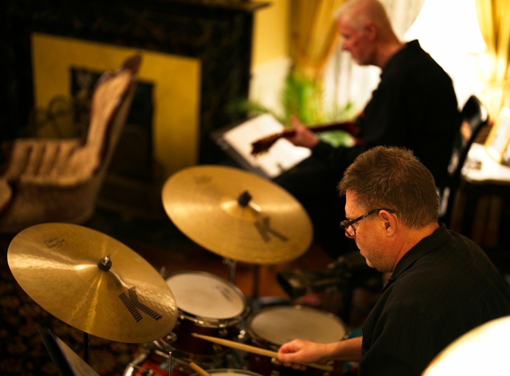 A man is playing drums while another man plays a keyboard