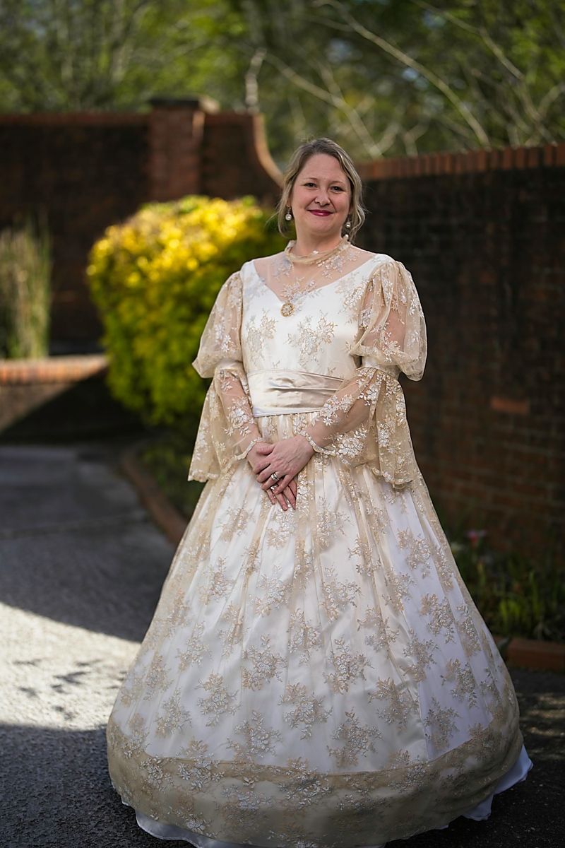 A woman in a white and gold dress is standing in front of a brick wall.