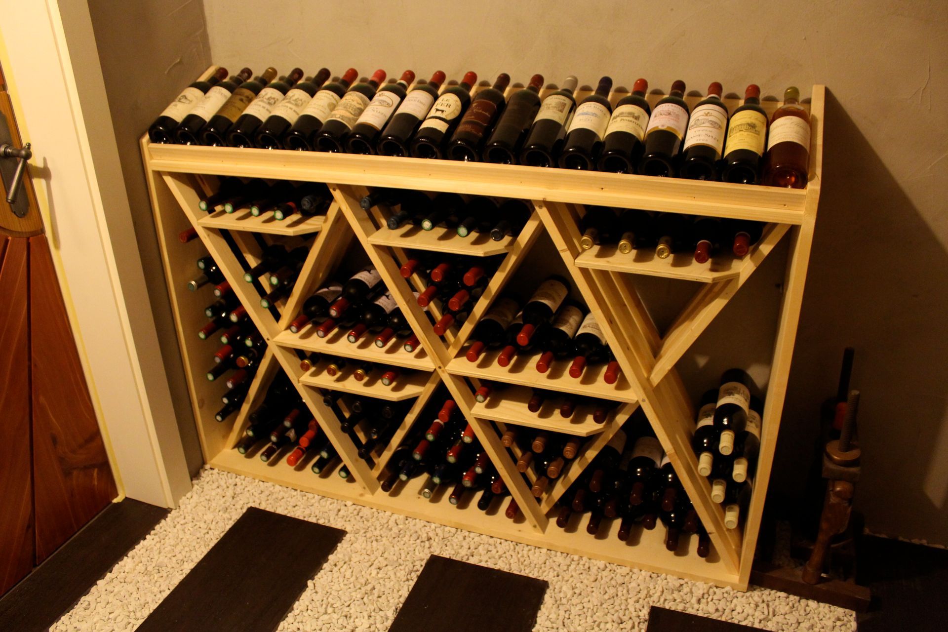 Casier à vin en bois rempli de bouteilles de vin, posé sur un sol en galets et en carrelage.