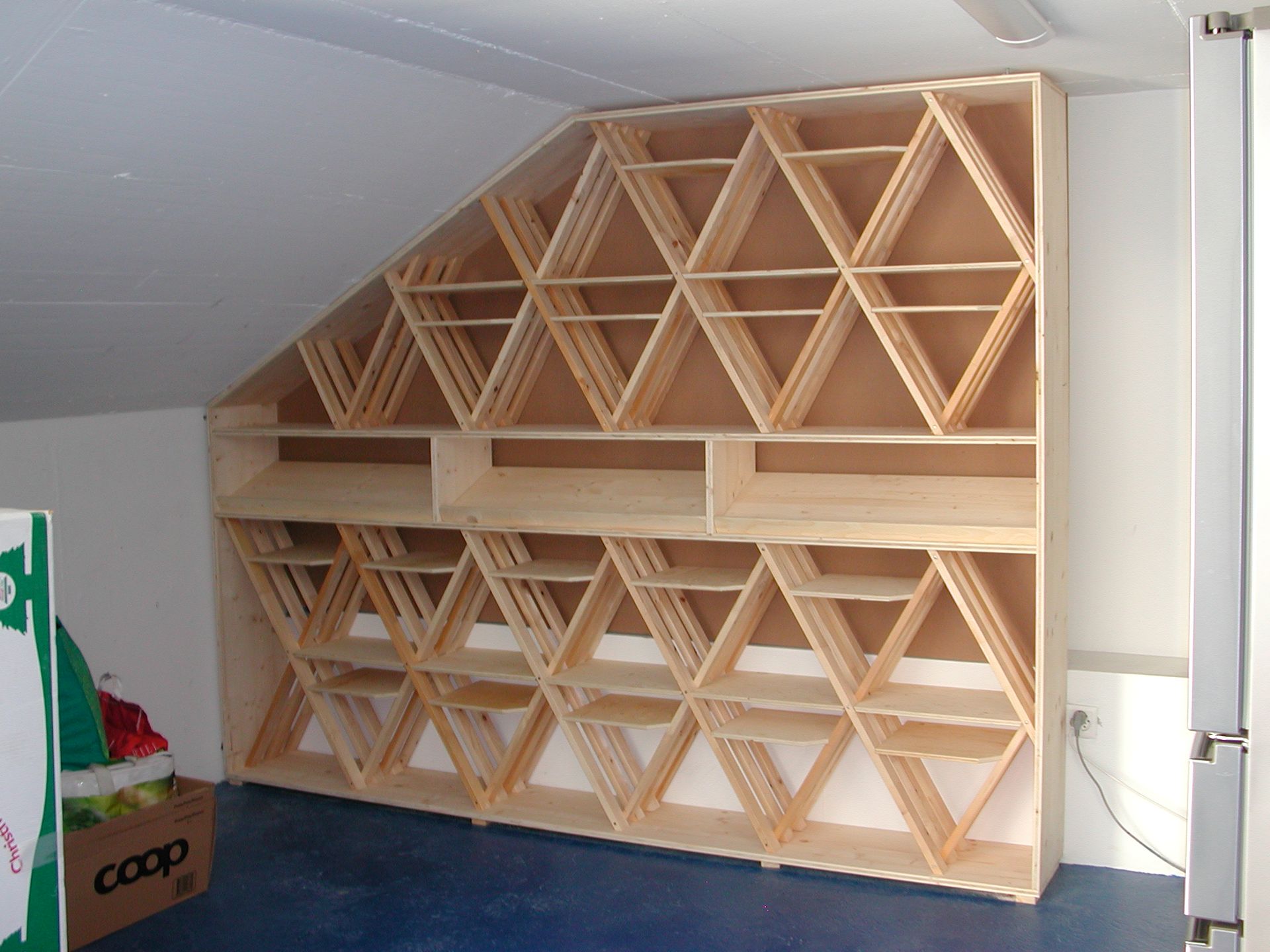 Casier à vin en bois intégré dans un mur en angle, avec des sections de rangement hexagonales et triangulaires.