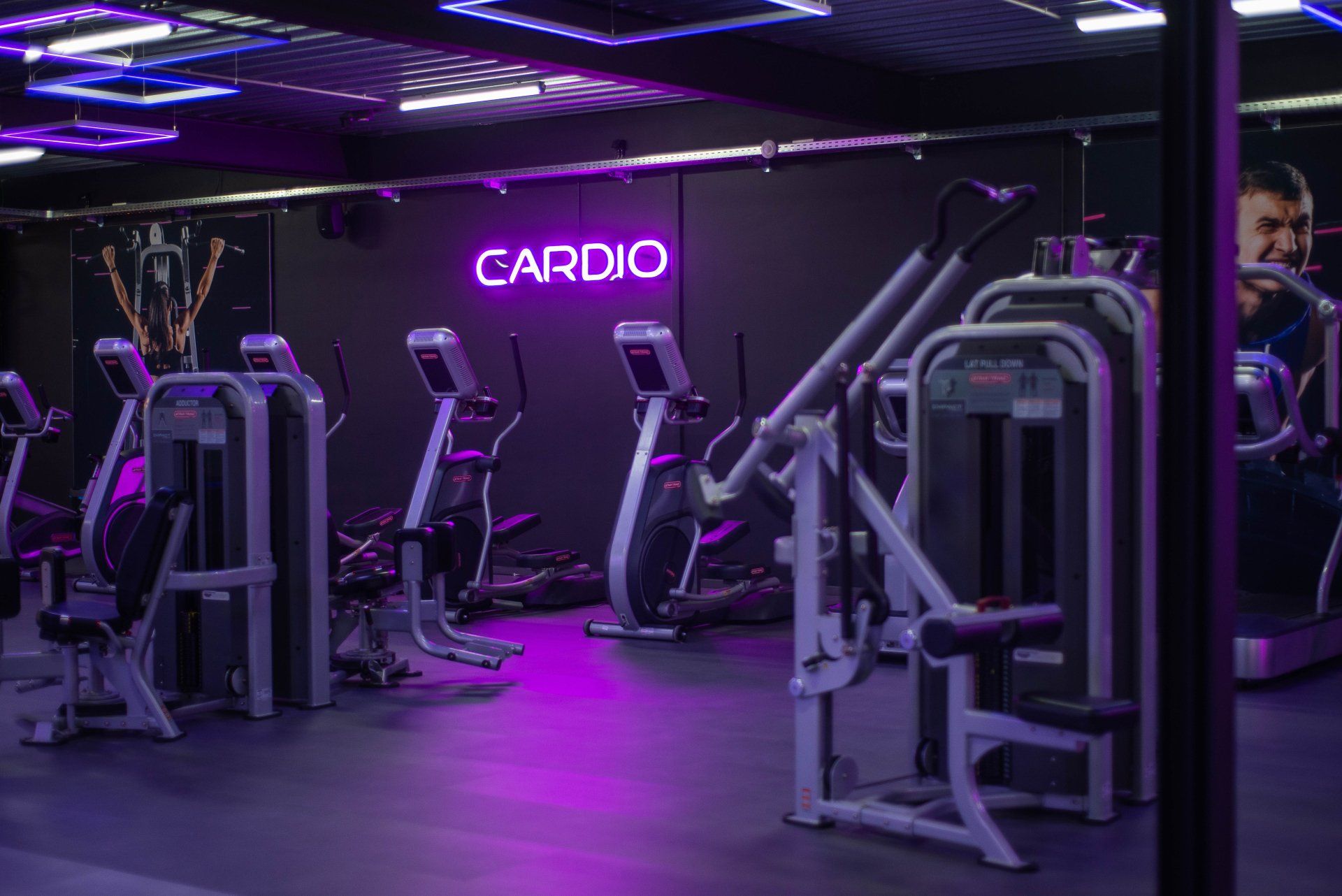 Een sportschool met veel fitnessapparatuur en een neonbord met de tekst cardio.