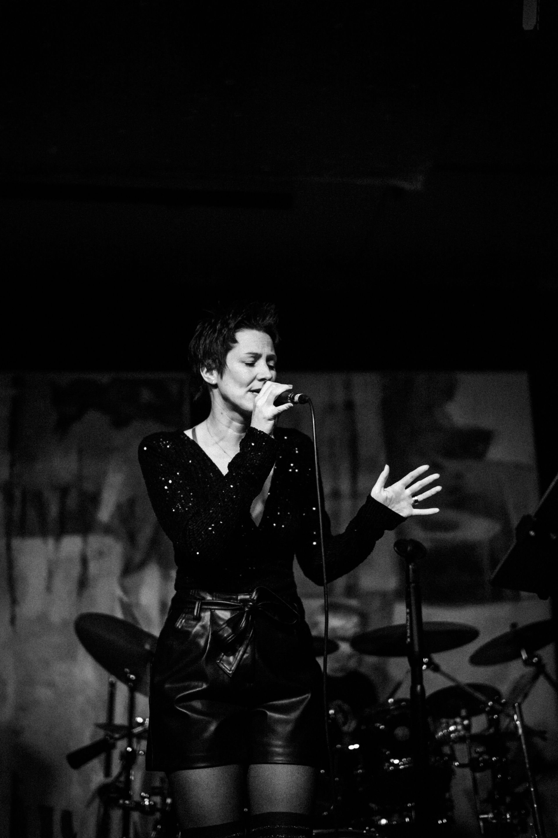 Auf einem Schwarz-Weiß-Foto singt Natalia Salamin auf einer Bühne in ein Mikrofon.