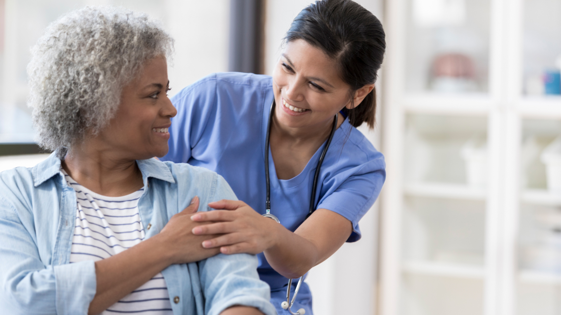 quality life services nurse in blue scrubs assisting elderly patient