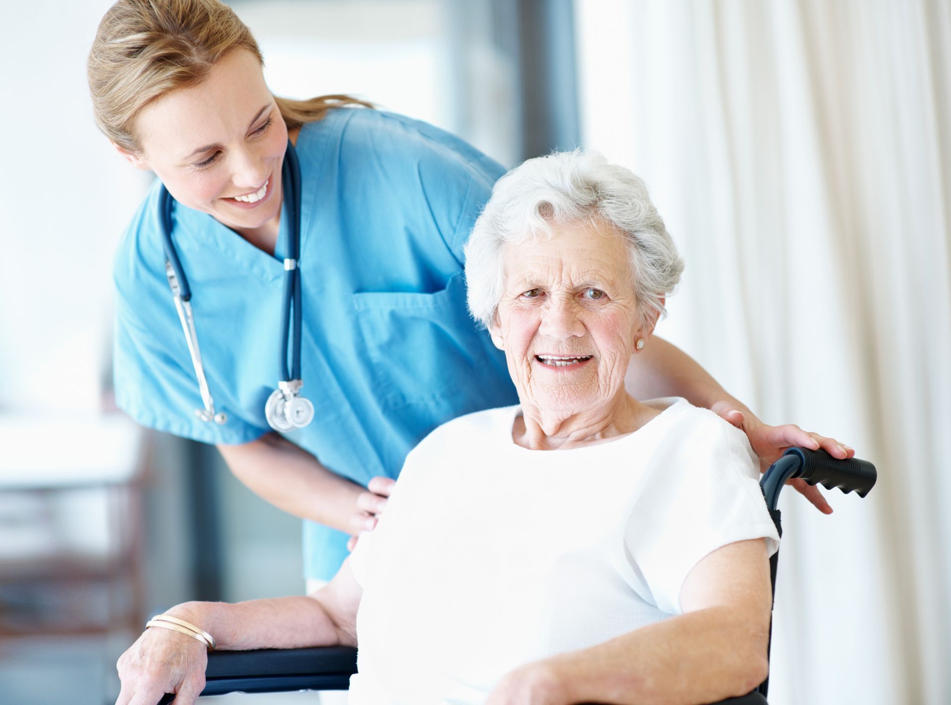 female nurse in scrubs pushing elderly patient in wheelchair at Quality Life Services Nursing Home in Western, PA