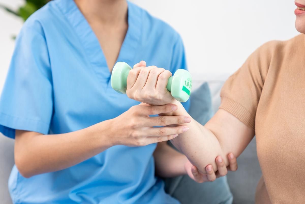 Caregiver helping contented senior woman exercise with dumbbell