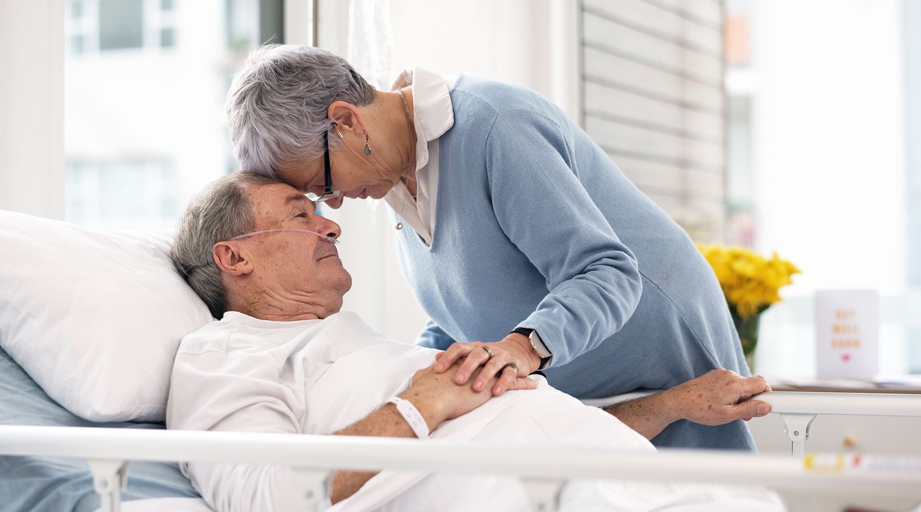 woman hugging sick husband in hospital bed