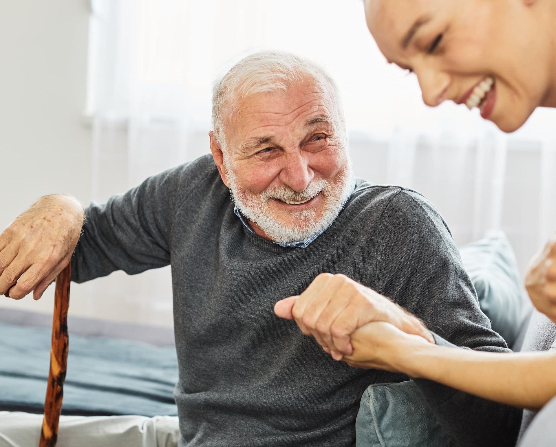 image of elder man with a cane getting ready to stand up with assistance from a younger woman 