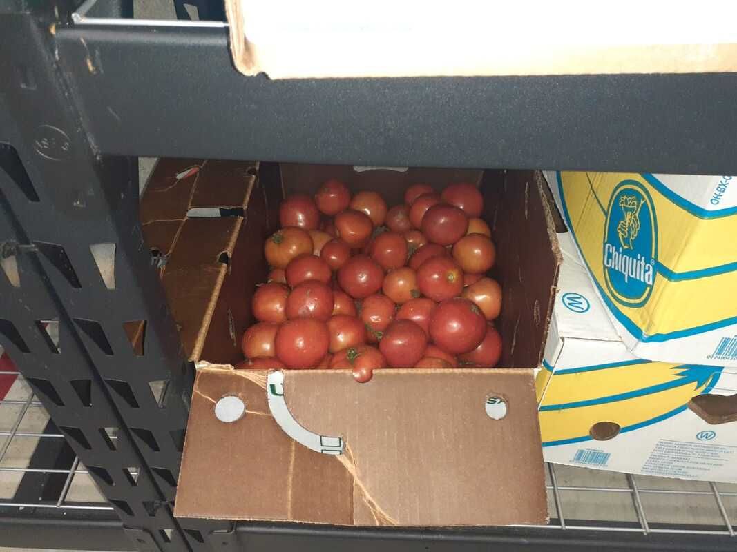 A box of tomatoes sits on a shelf next to a box of bananas
