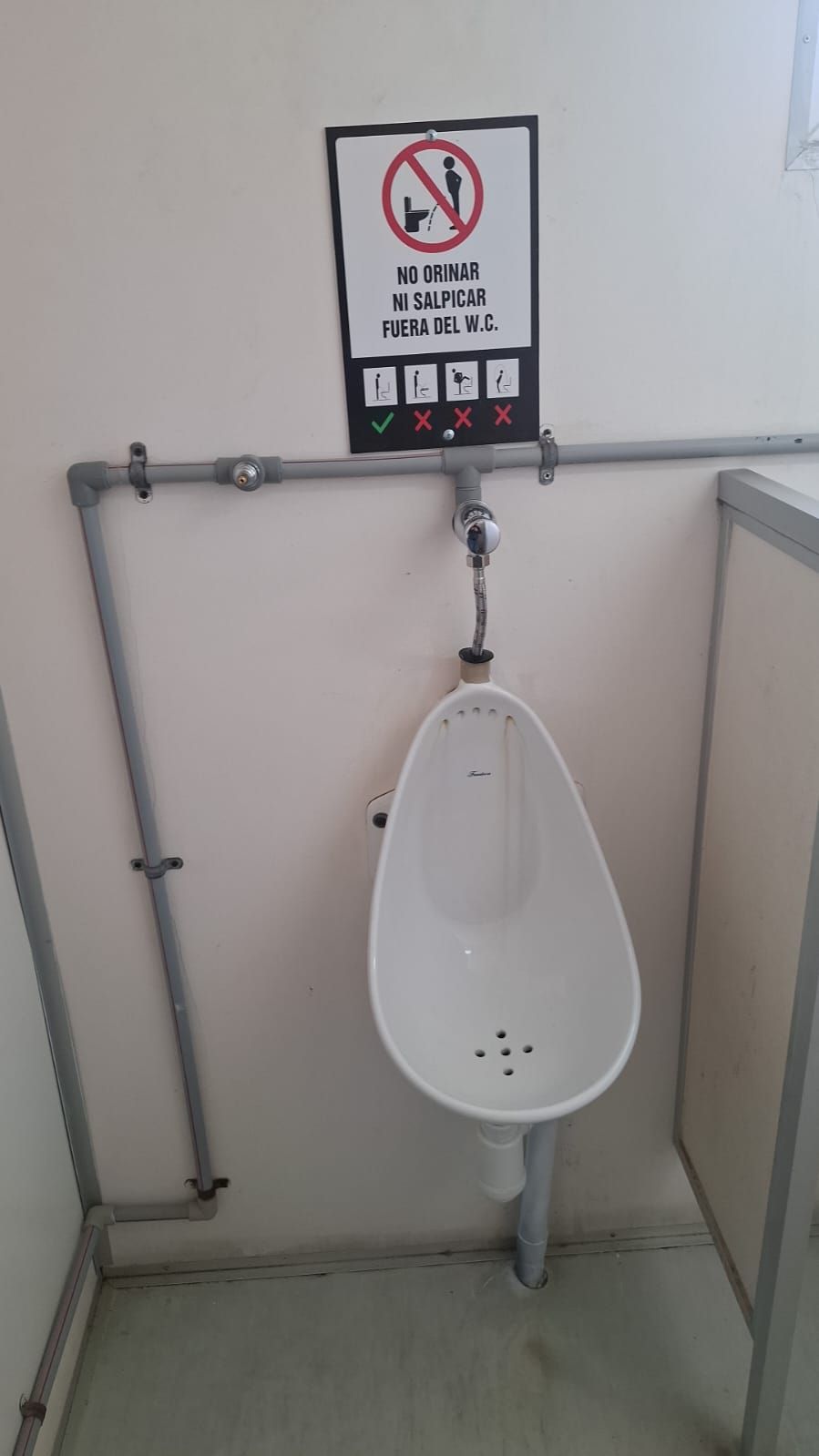 Urinario en un baño público con un cartel que prohíbe orinar fuera del urinario.