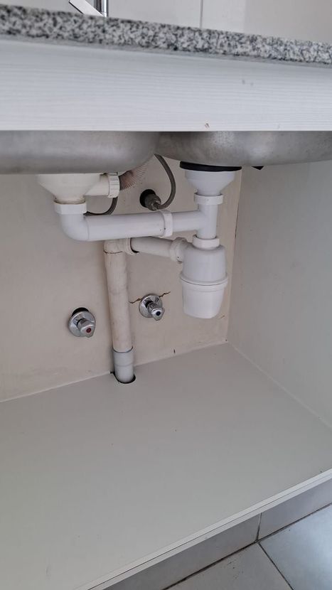 Instalación de plomería de fregadero de cocina blanco debajo de un gabinete.