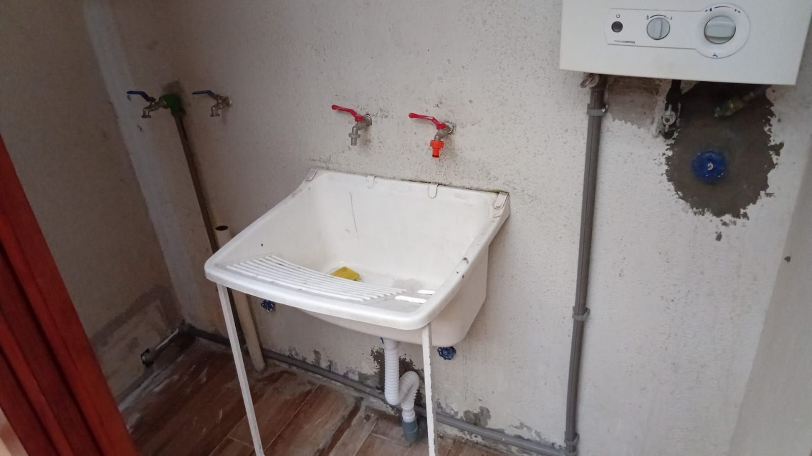 Lavandería con fregadero blanco, dos grifos y caldera de gas montada en la pared.