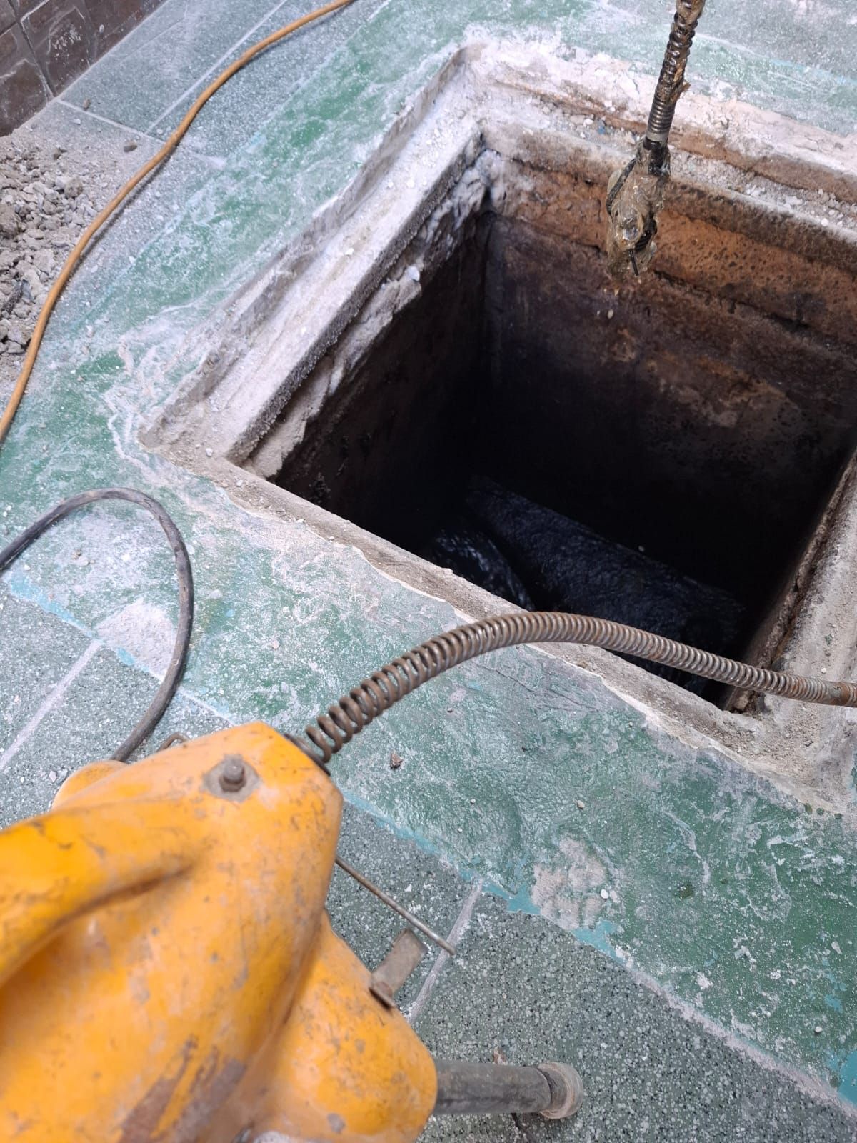 Una abertura cuadrada de hormigón verde, con una herramienta amarilla en primer plano