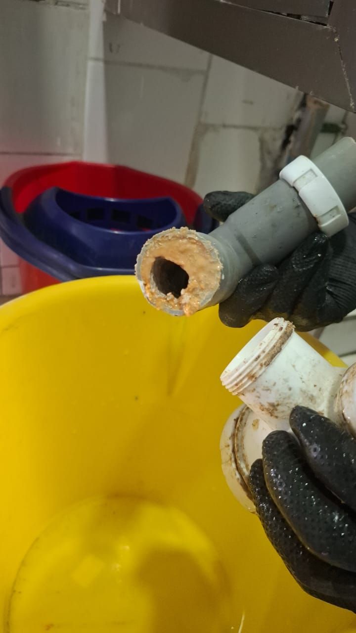 Manos sujetando un desagüe de fregadero desmontado y muy obstruido.