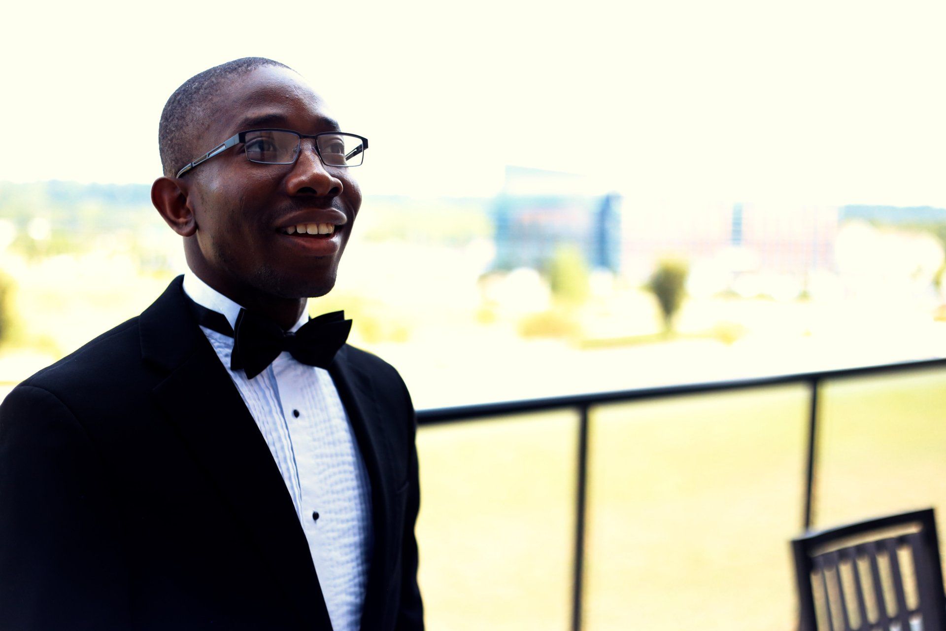 A man in a tuxedo and bow tie is standing on a balcony.