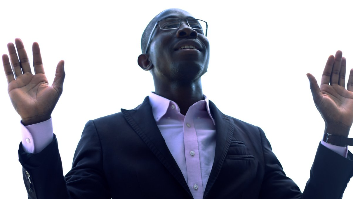 A man in a suit and glasses is raising his hands in the air.