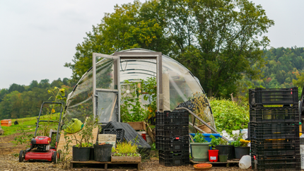 A greenhouse filled with potted plants and a lawn mower in a field.