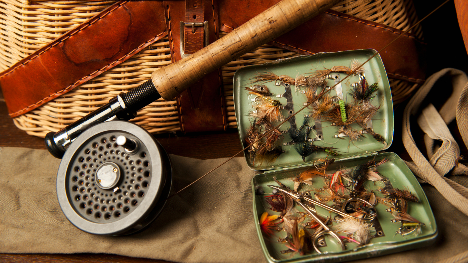 A fly fishing rod and reel are on a table next to a basket.